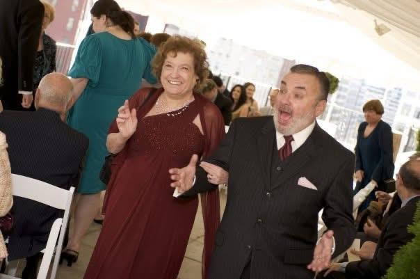 A couple joyfully dances together while guests celebrate at a beautiful rooftop wedding.