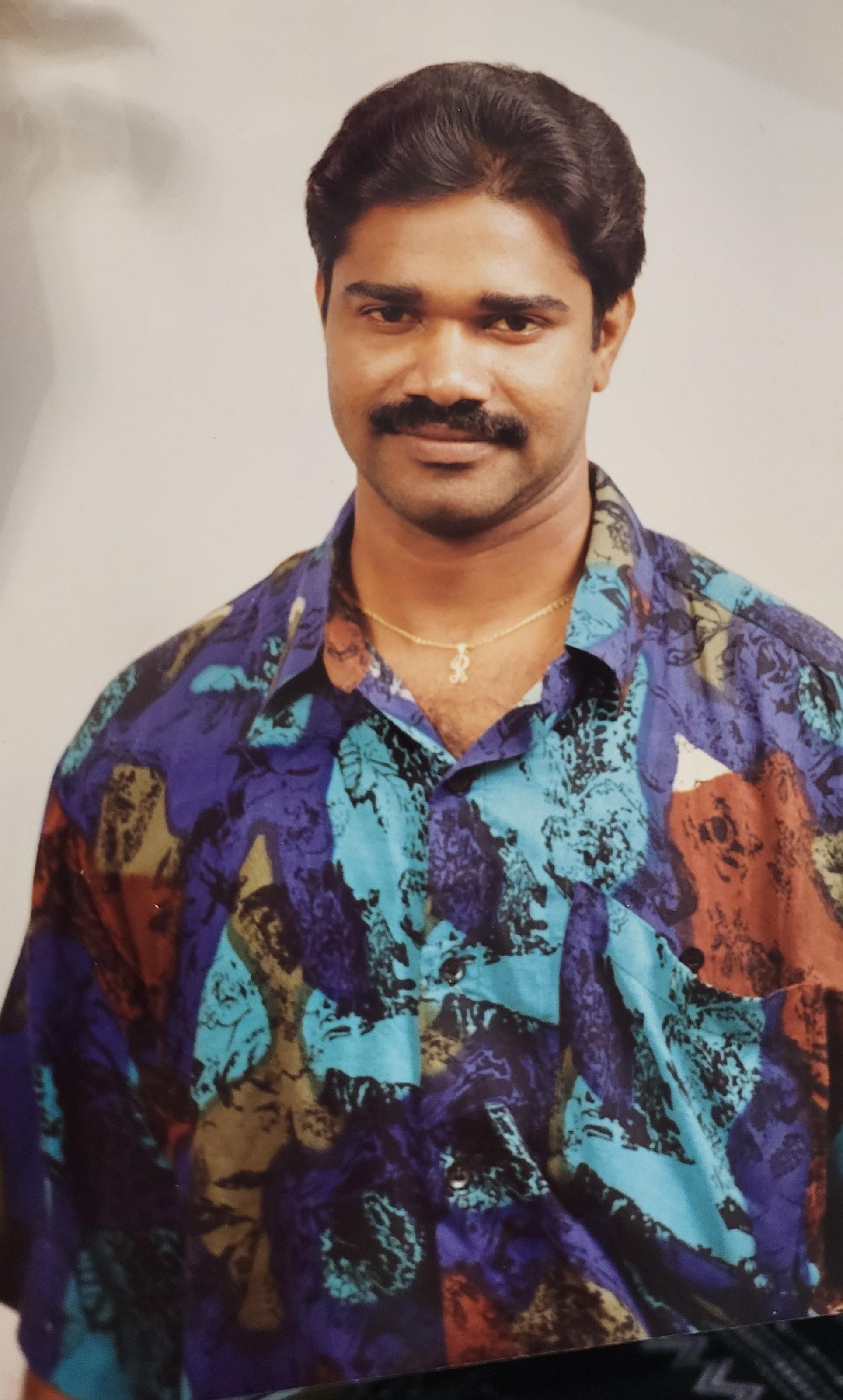 A man poses confidently in a colorful patterned shirt, showcasing a friendly smile.