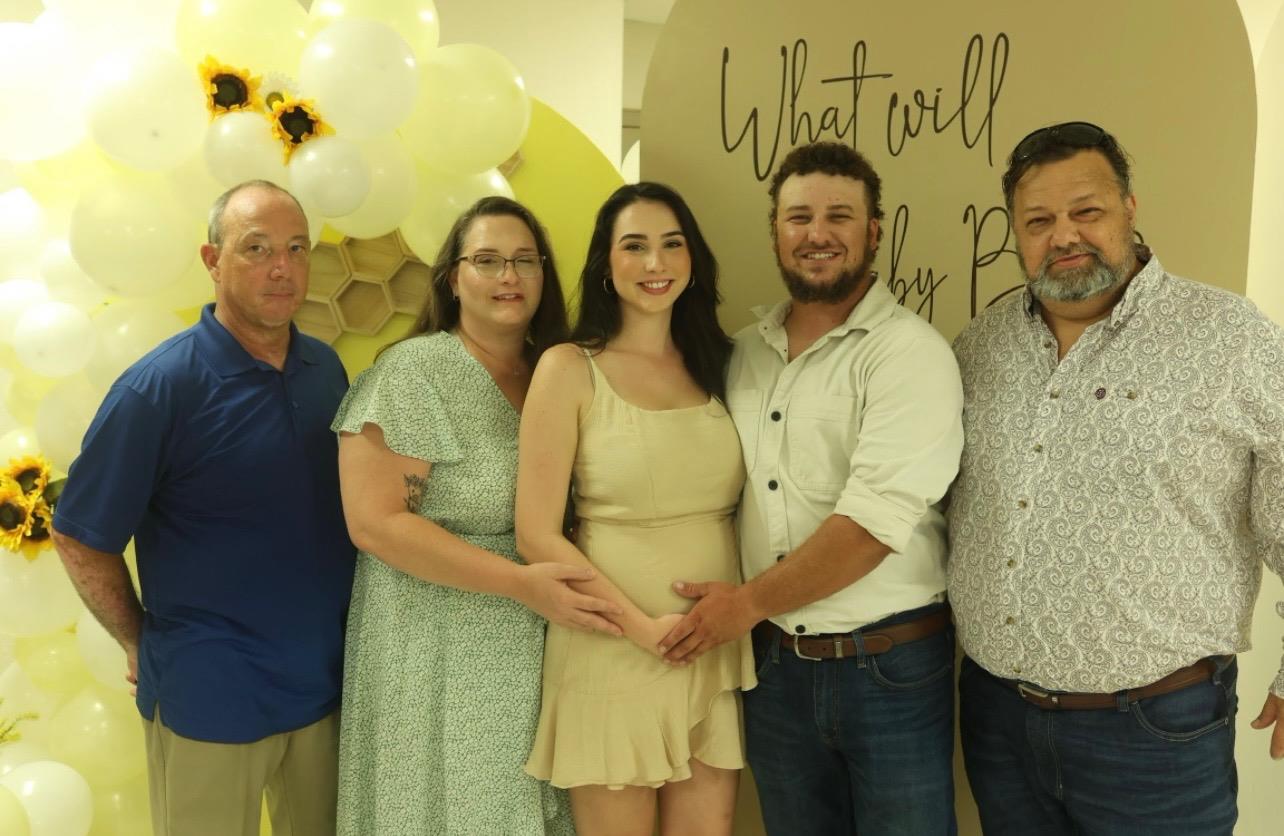 Expectant parents stand proudly with family members at a vibrant baby shower celebration.