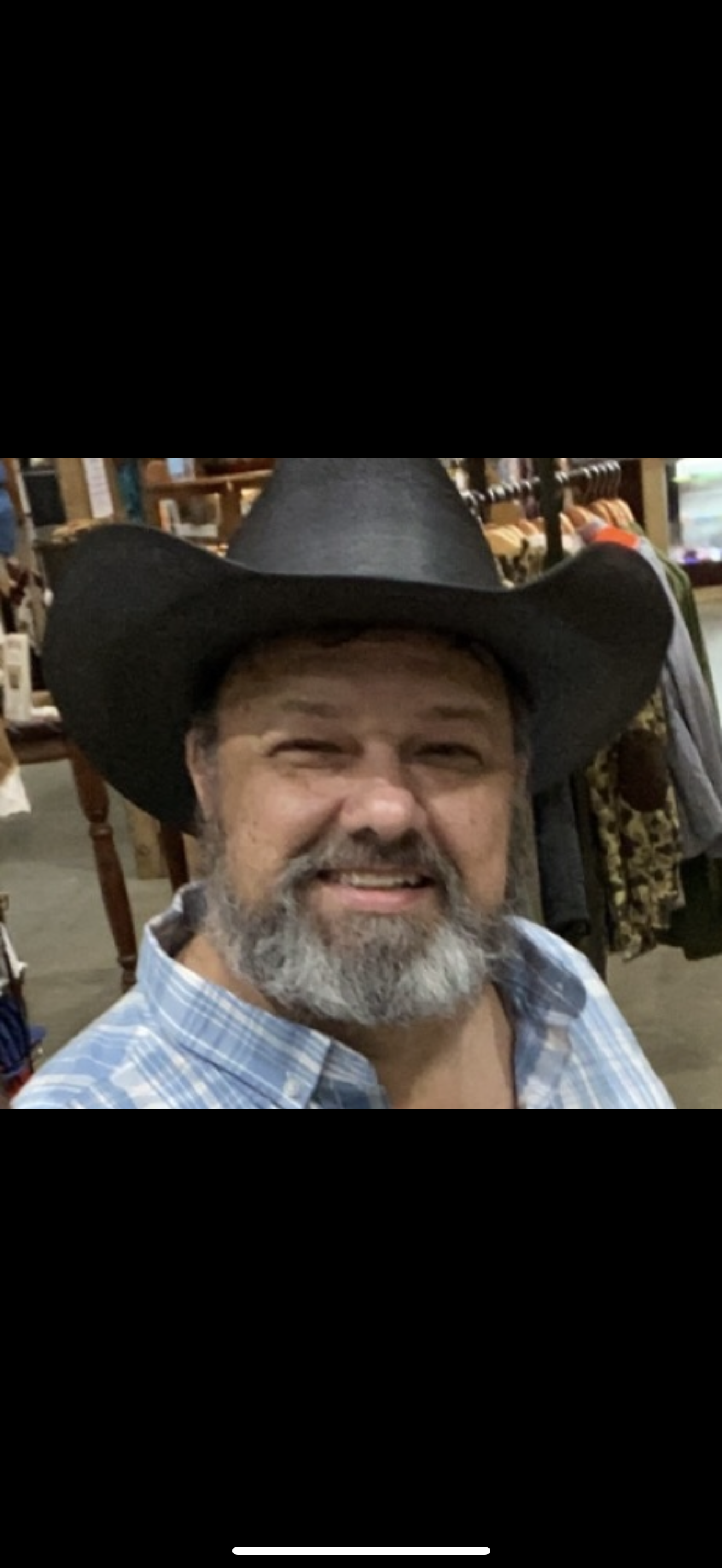 A man with a beard and a cowboy hat smiles while posing in a charming western-themed shop.