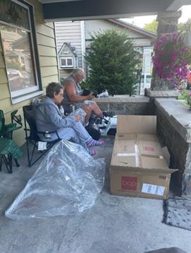 Two individuals sit casually on a porch, unpacking boxes and enjoying the outdoors in summer.