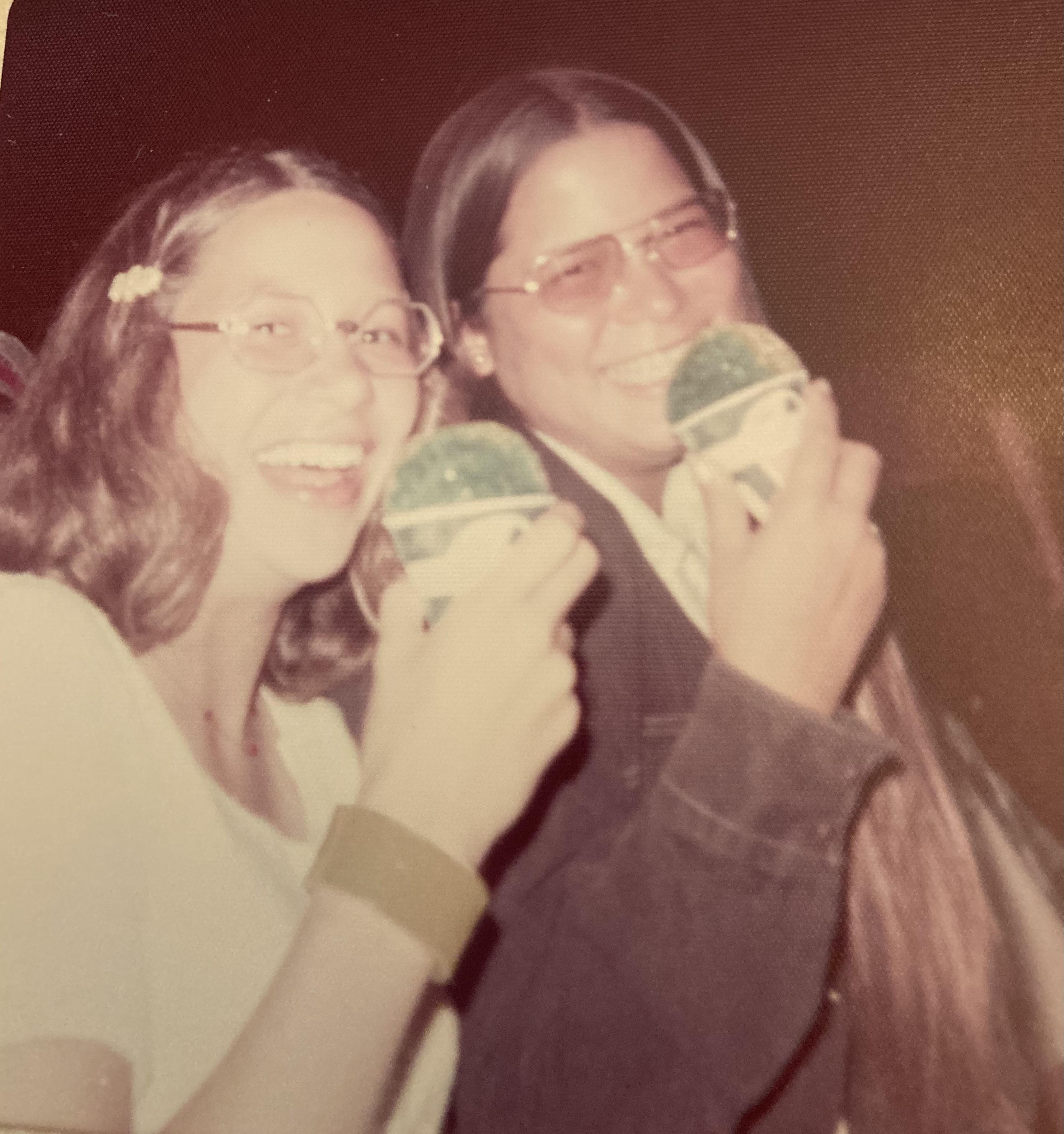 Two friends smile brightly while holding vibrant frozen desserts during a nighttime outing.