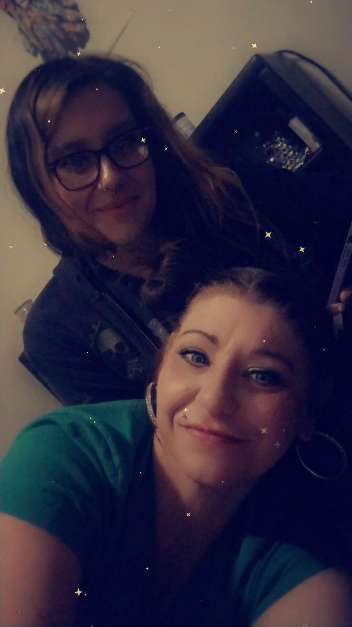 Two friends pose for a cheerful snapshot in a cozy indoor space while enjoying each other's company.