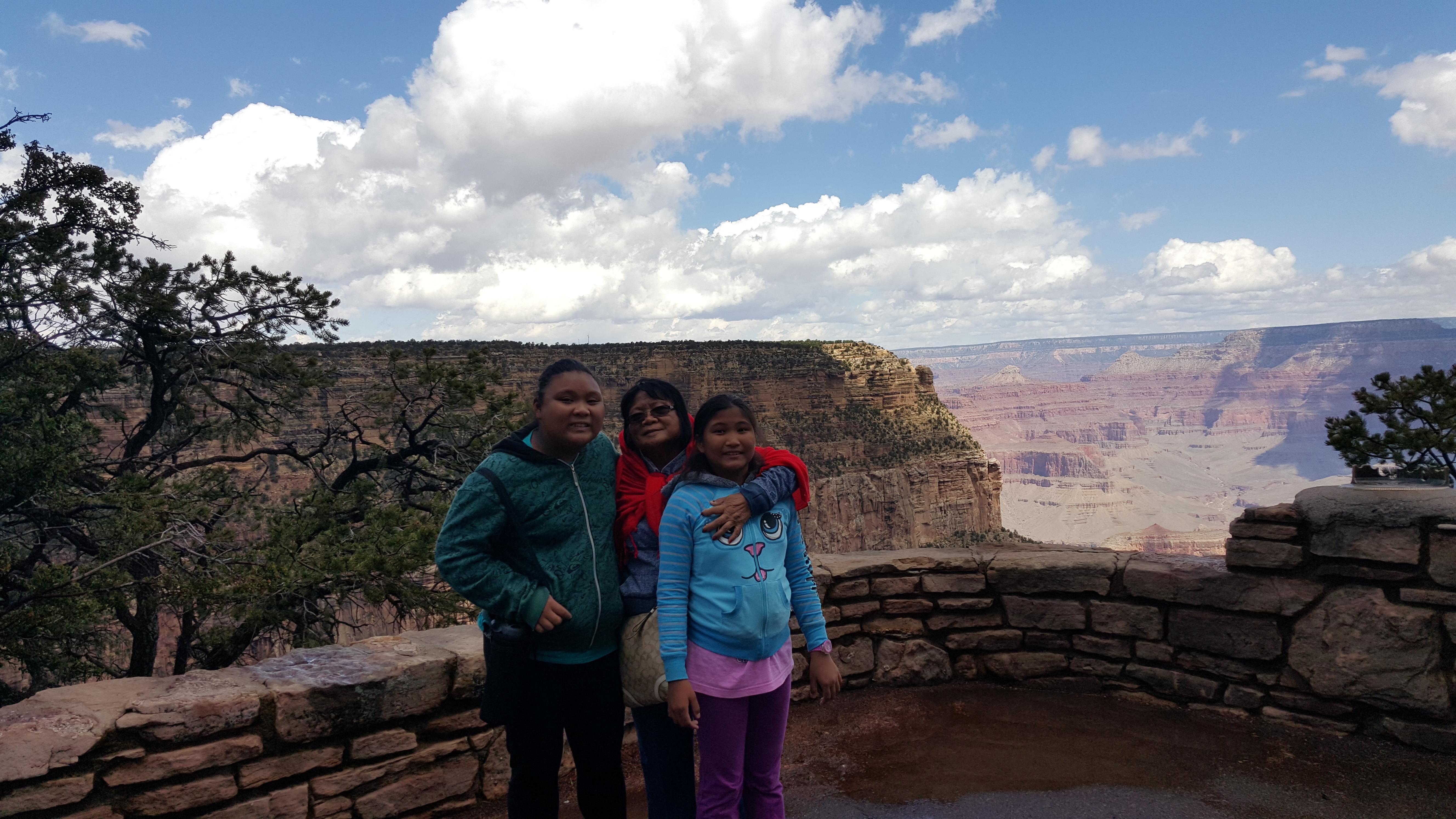 Three children smile while posing against the Grand Canyon backdrop on a clear day.