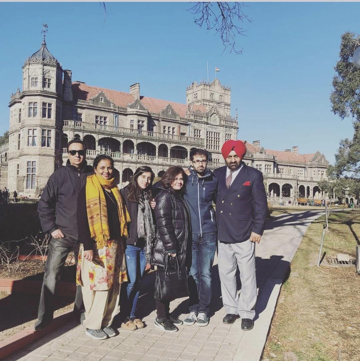 Six friends smile together in front of a stunning historic building and gardens.