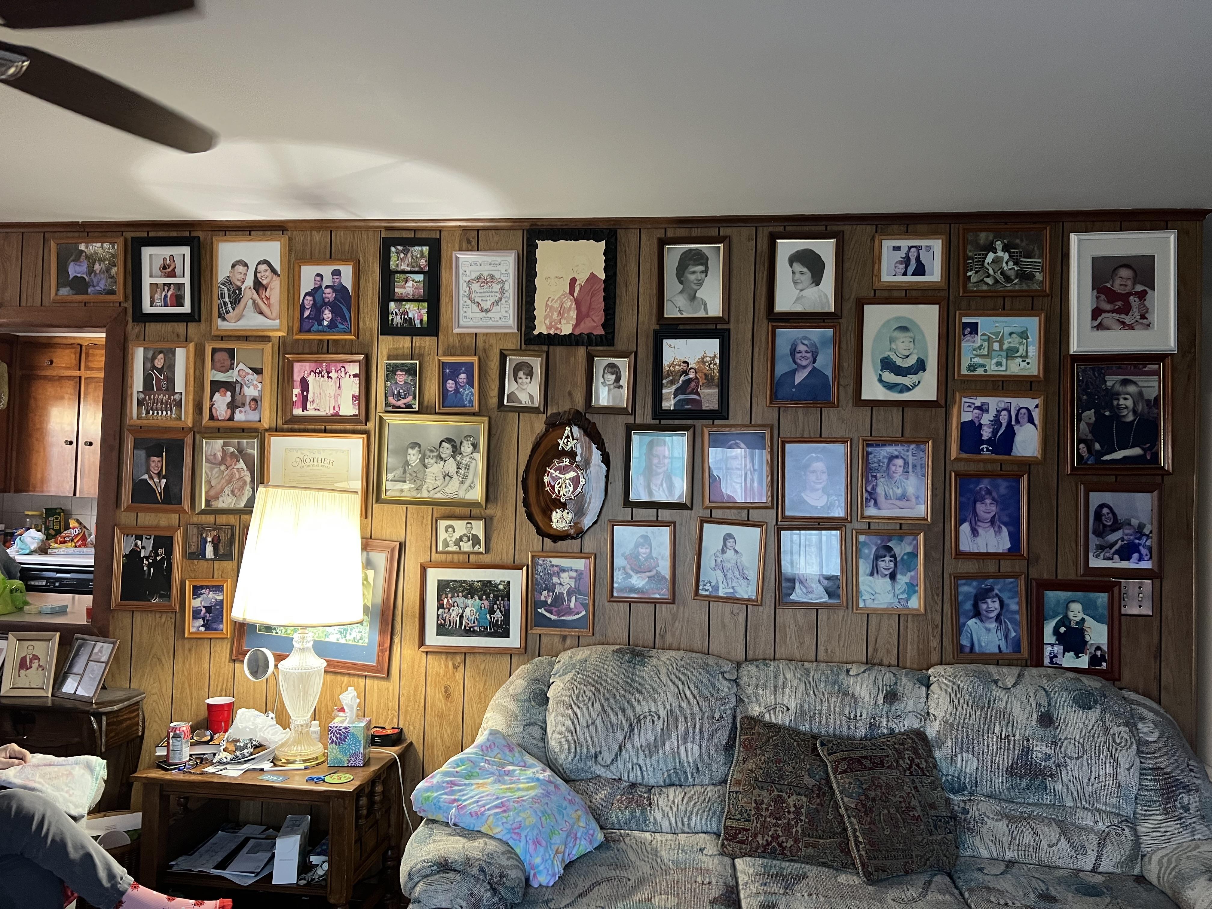 Numerous framed family photographs fill a wooden wall in a warm living room, showcasing memories.