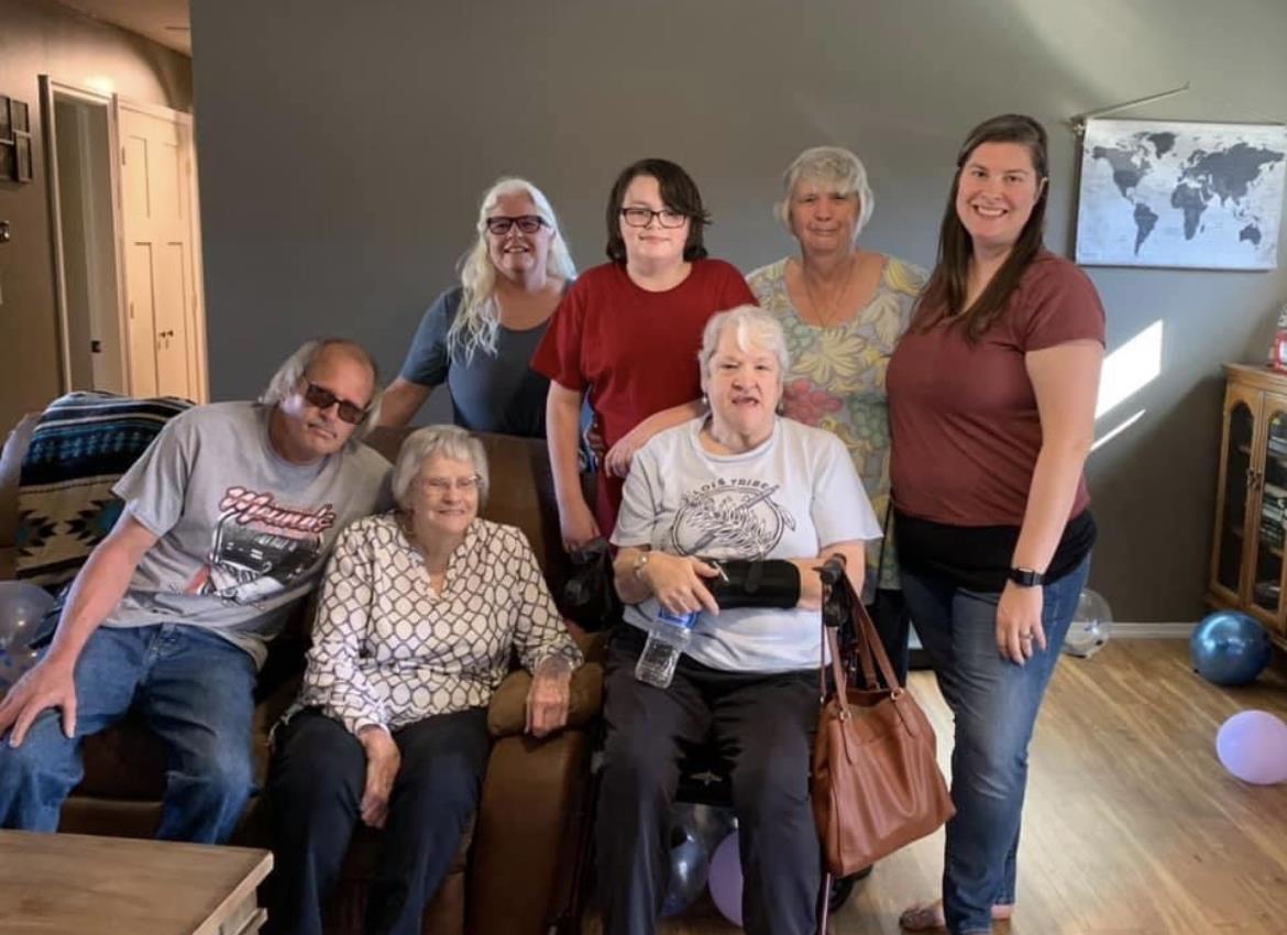 Eight family members smile together, sharing memories in a cozy living room.