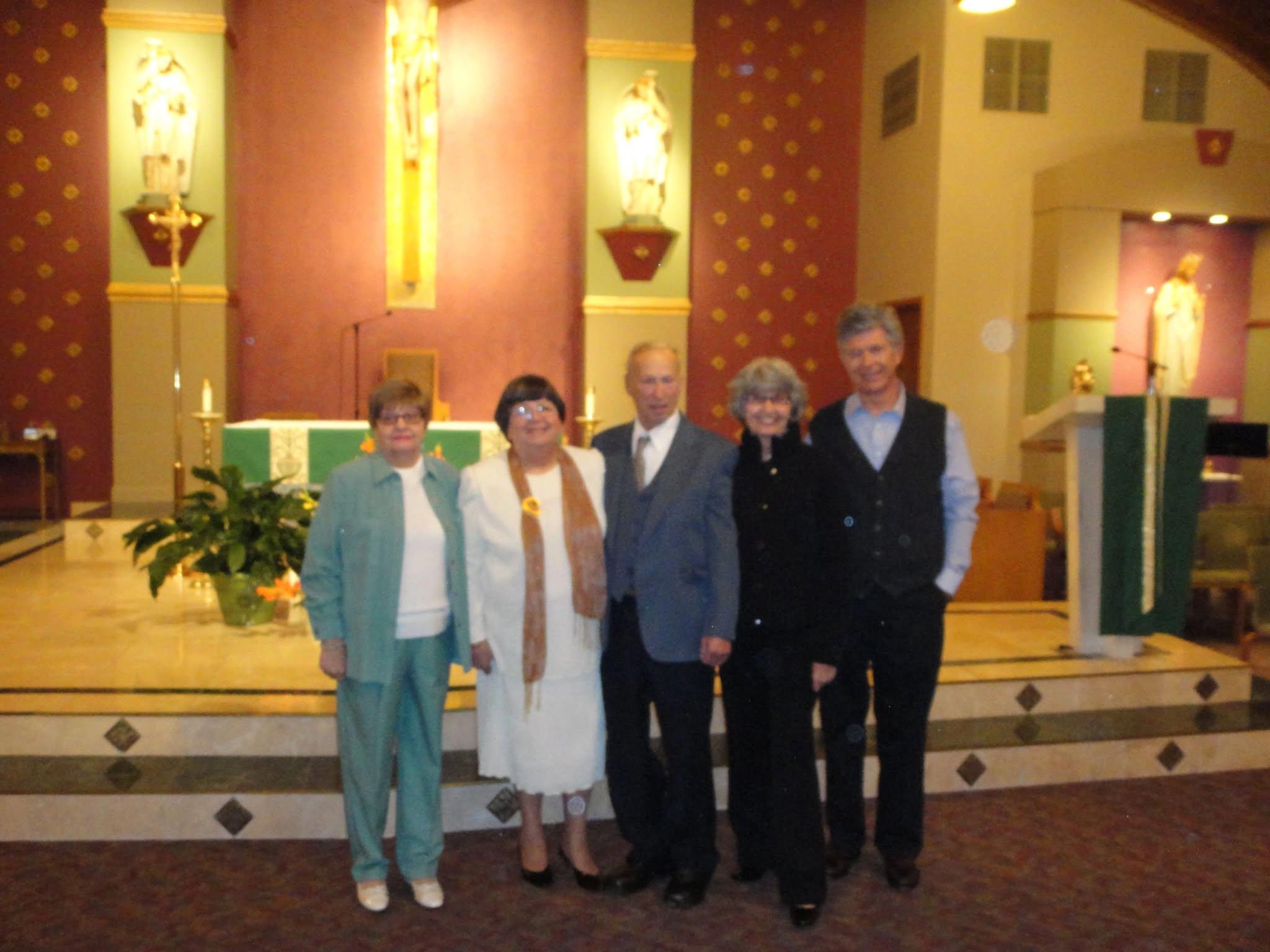 Five adults in formal attire stand together in a beautifully decorated church.