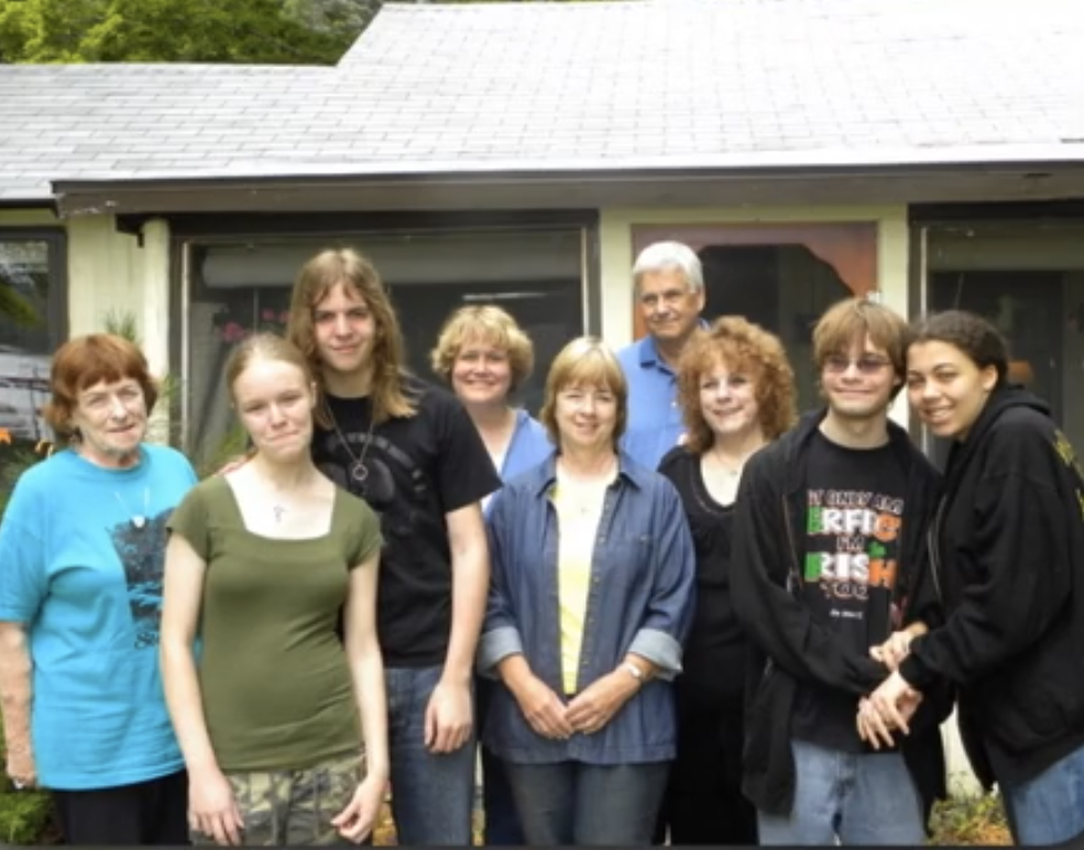 Eight family members pose together in front of a house, smiling and enjoying the moment.