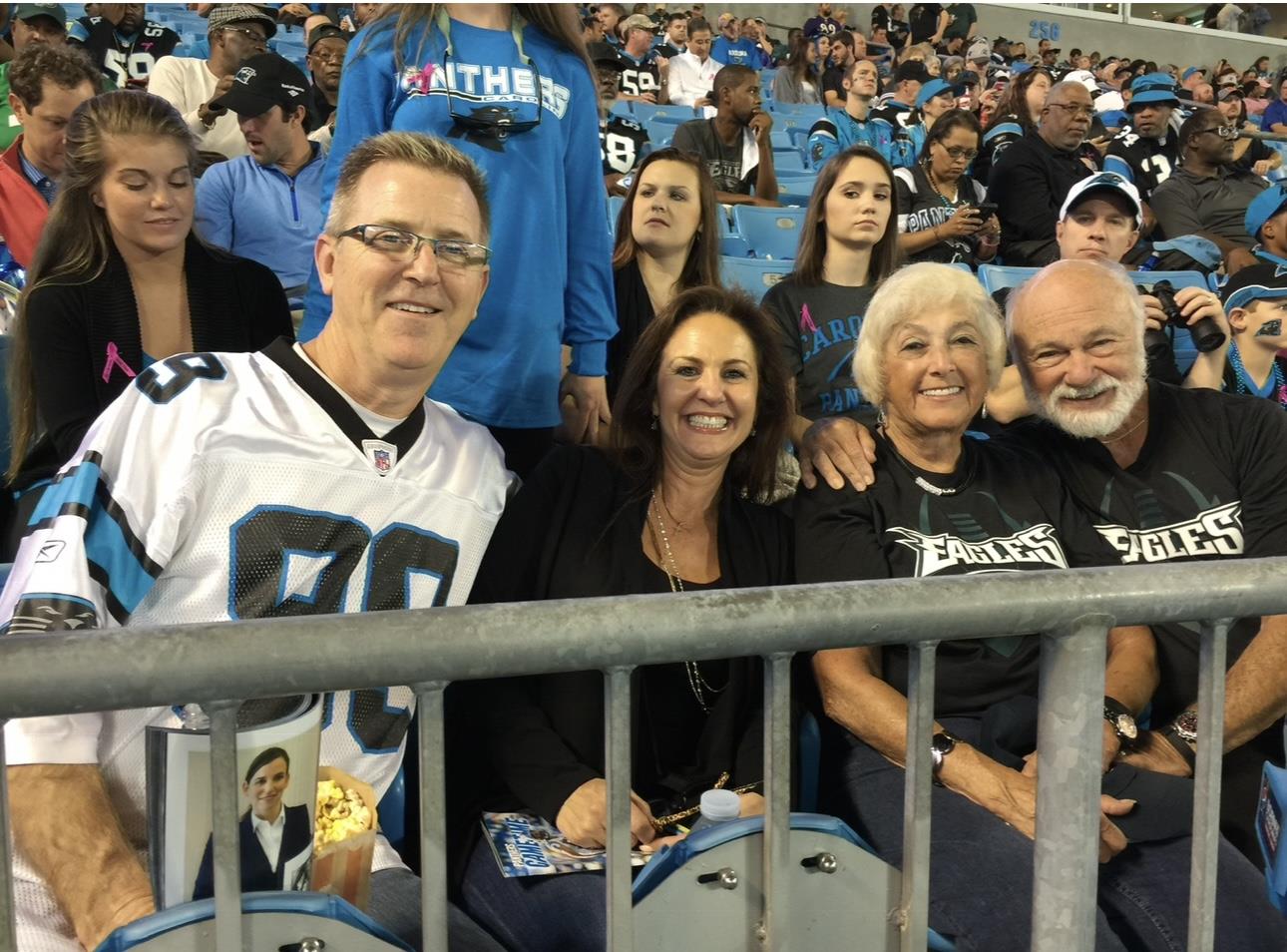 Four fans in jerseys celebrate together at the stadium, enjoying the game.