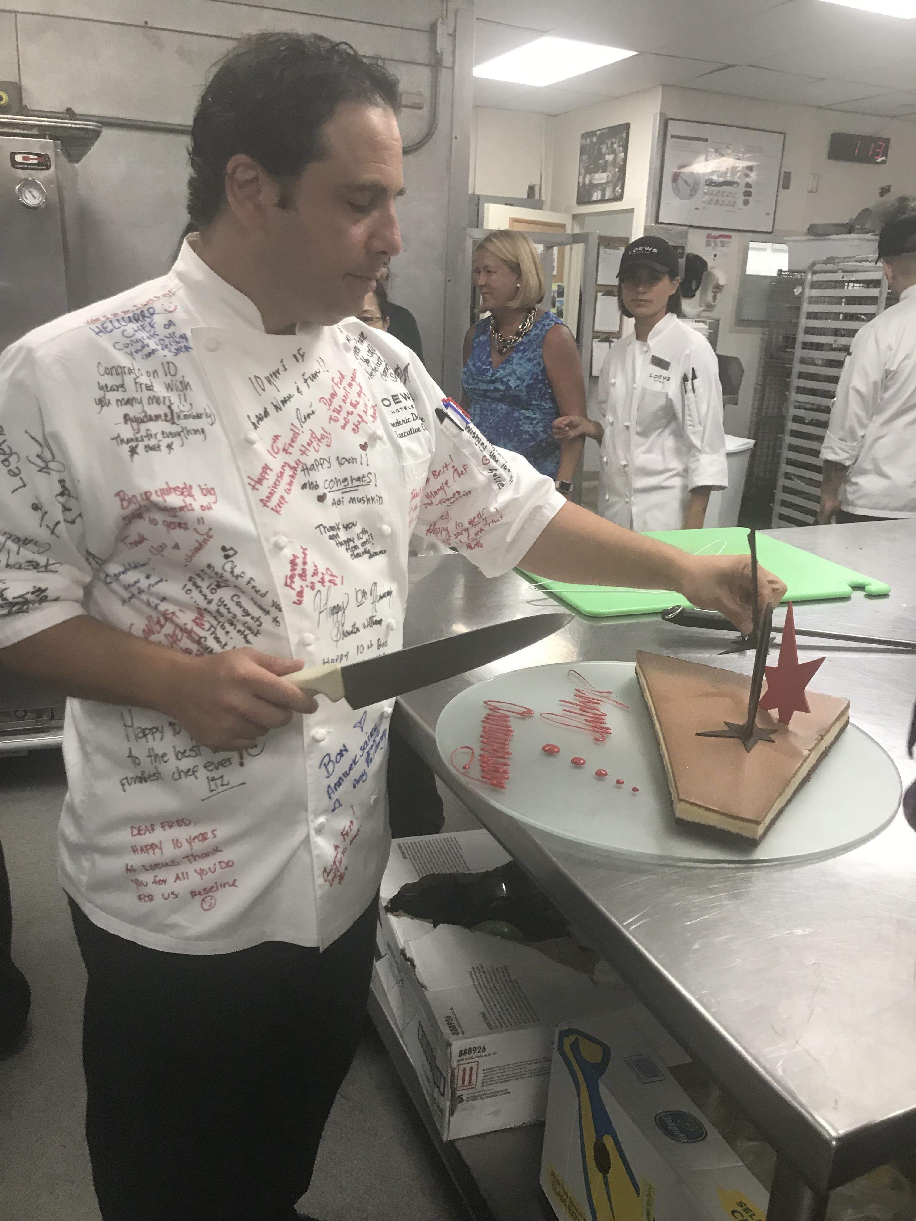 A chef focuses on decorating a cake with precision while students observe and learn nearby.