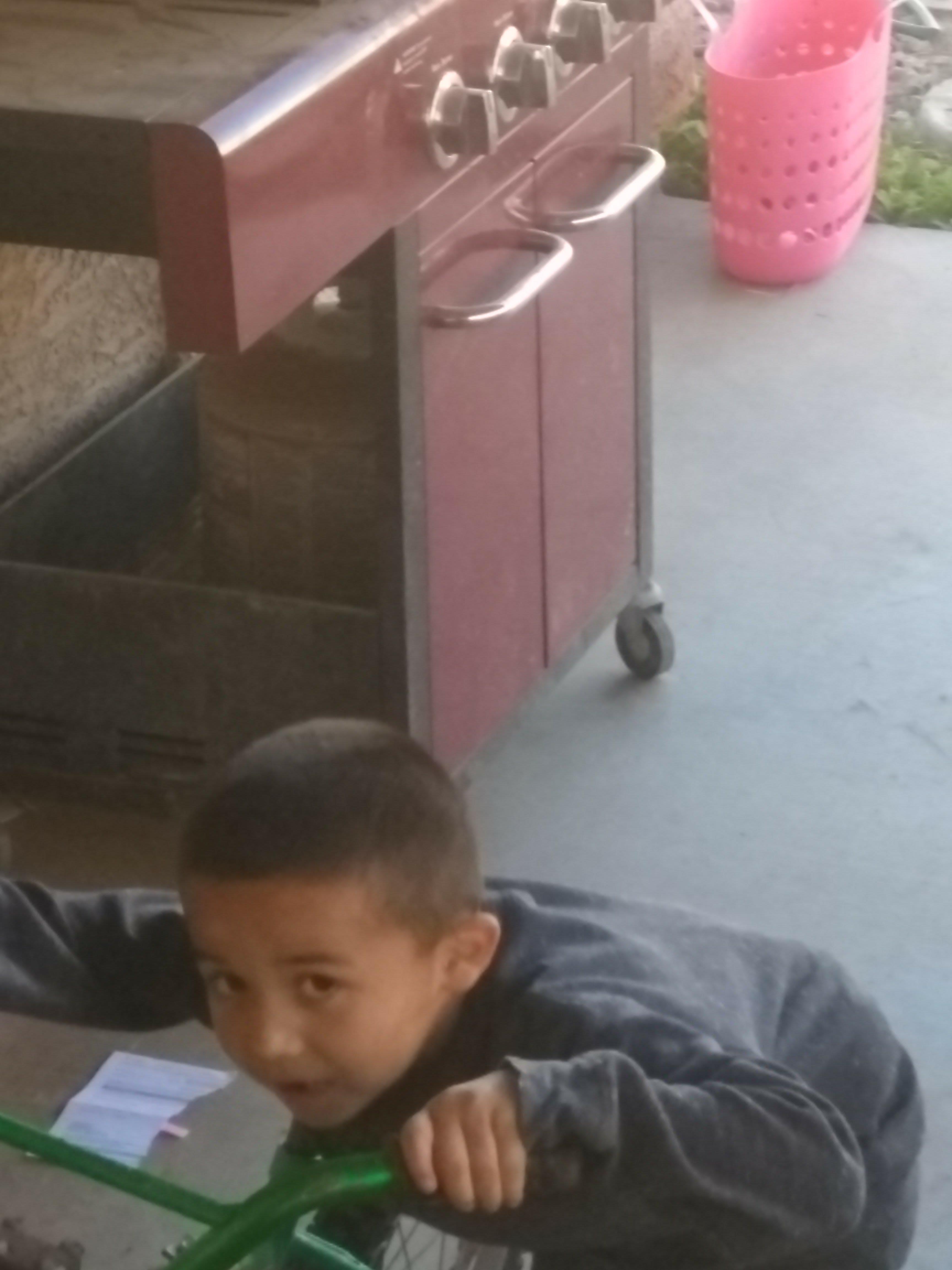A child is joyfully engaged with toys by a cart in a bright outdoor space, enjoying the day.