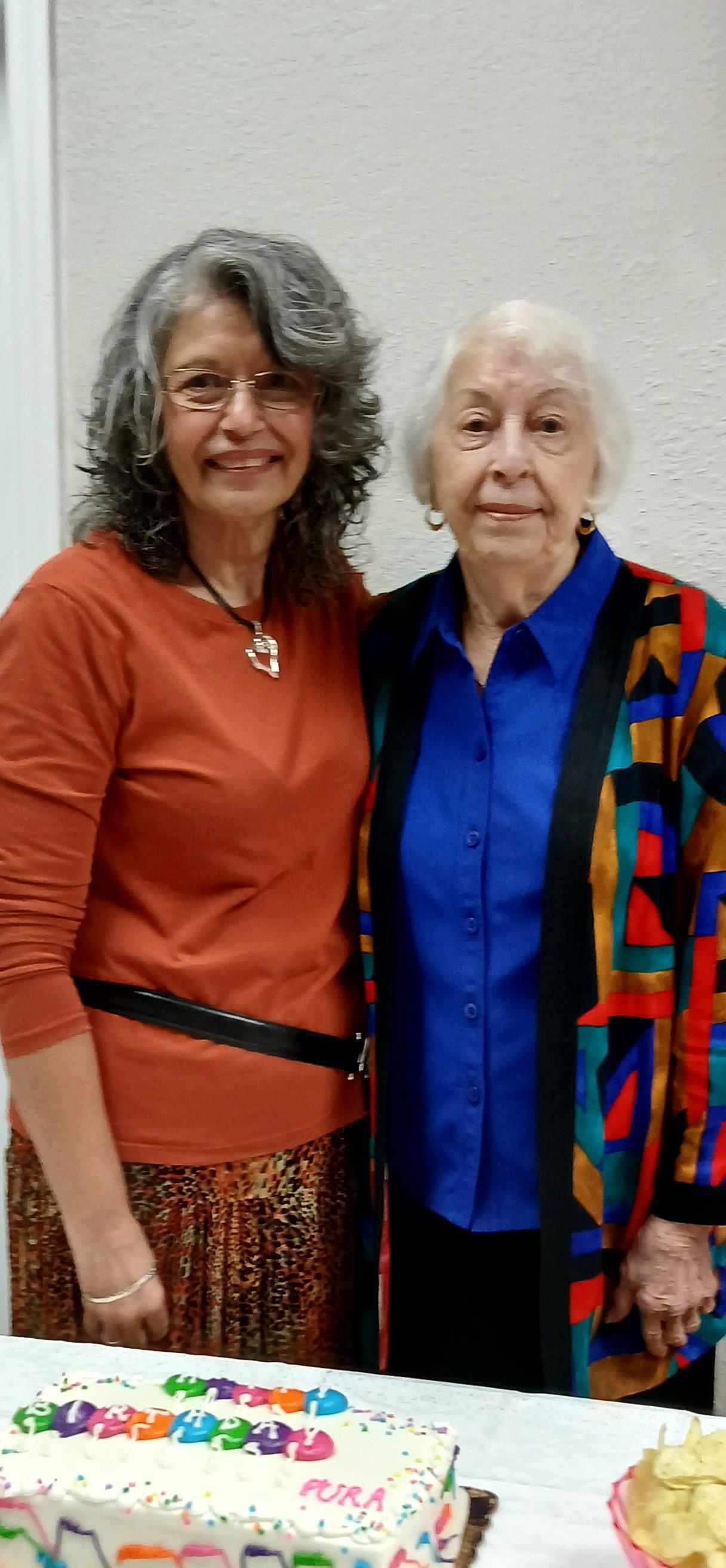 Two smiling women share a moment at a lively family celebration in a community space.