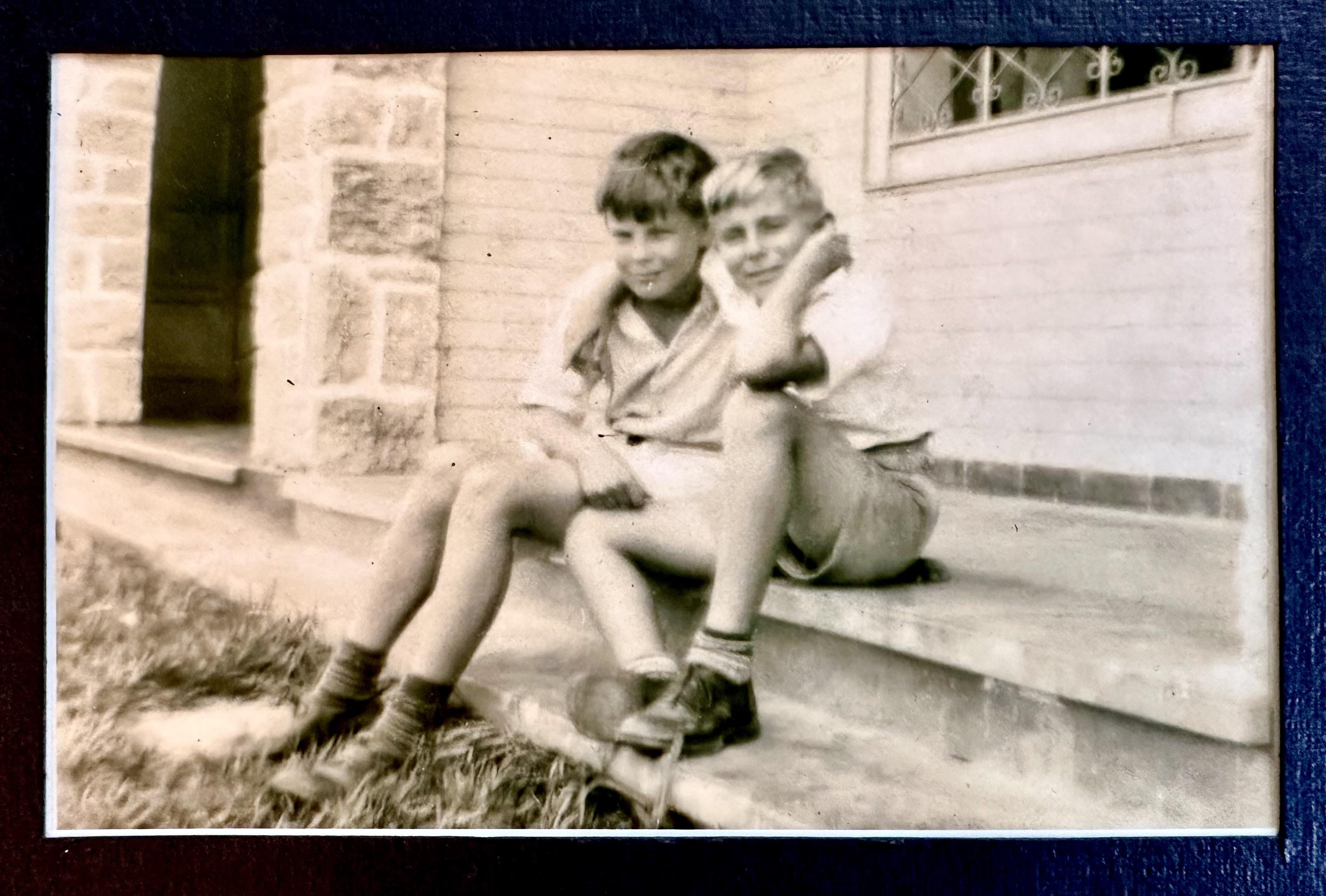 Two young boys relax on the steps of a stone building, enjoying a sunny day.