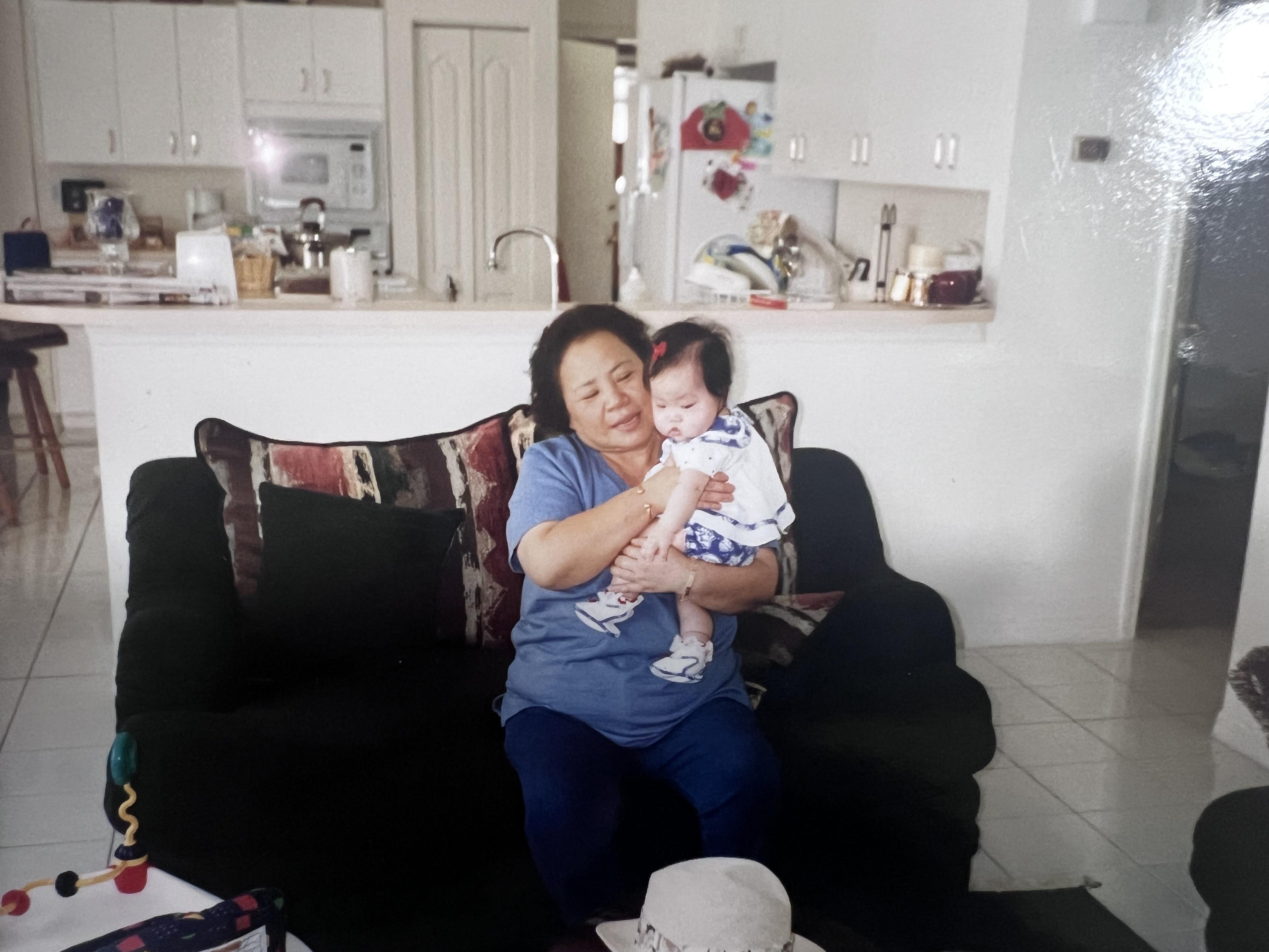 A grandmother lovingly holds her baby grandchild in a warm living room at home.