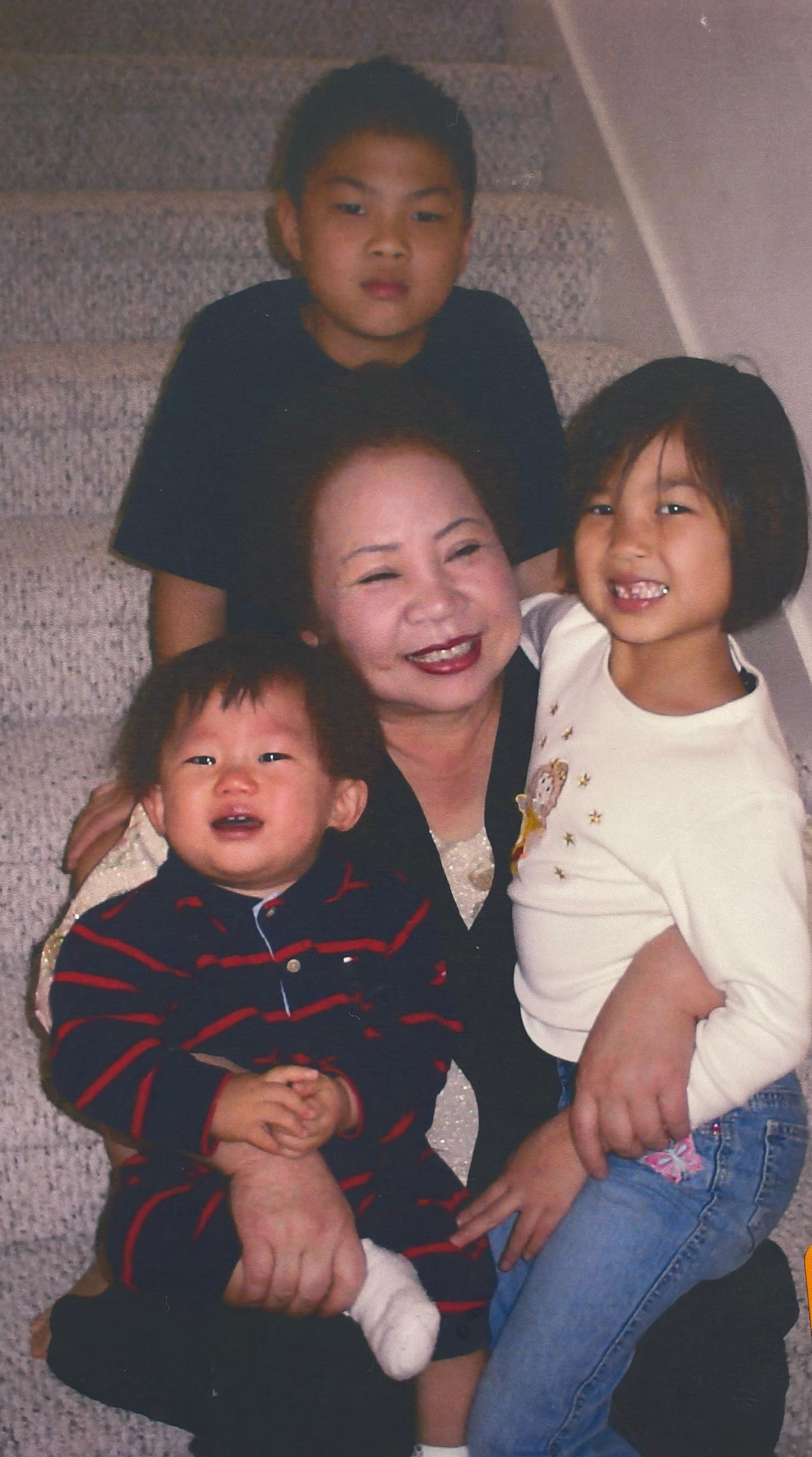 Children playfully gather around their grandmother, smiling and enjoying their time together.