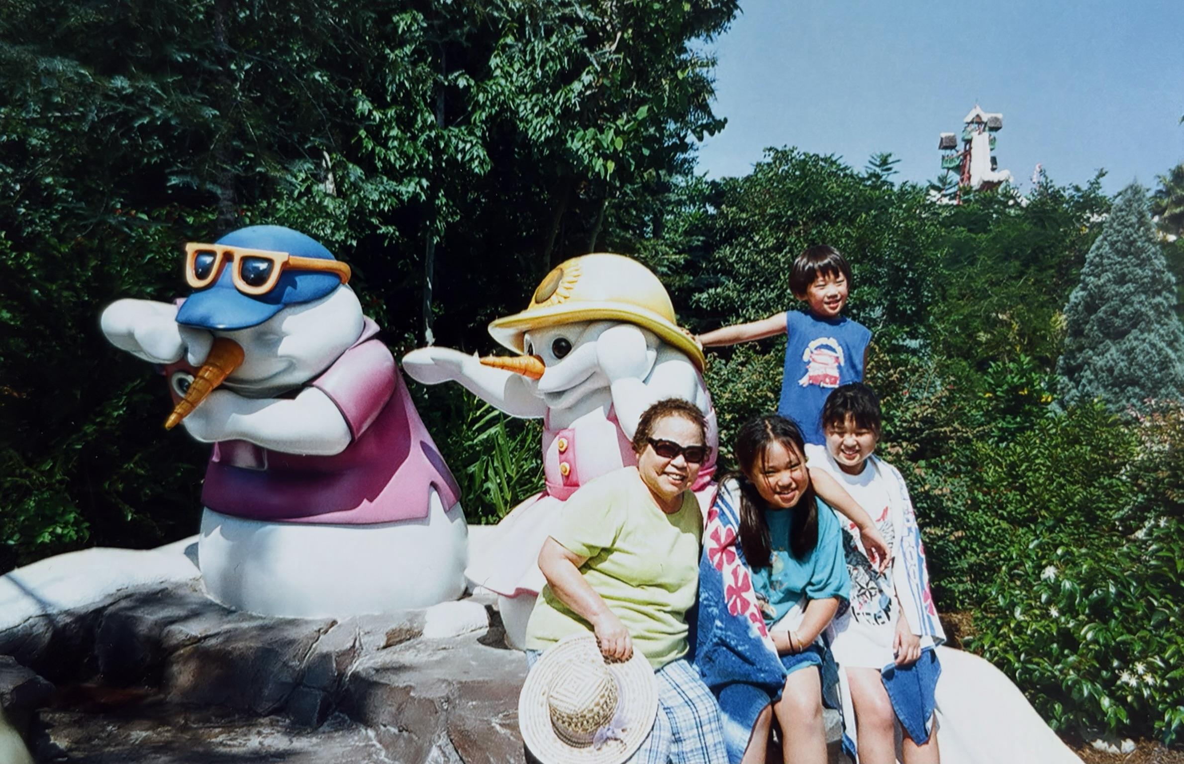 A group of children and adults pose together next to cheerful animal statues in a park.
