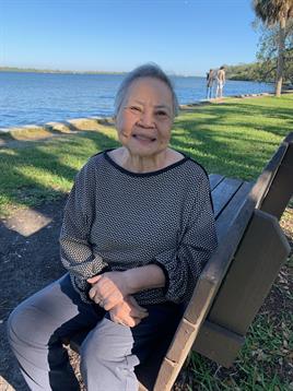 A cheerful elderly woman sits on a bench near the lake, enjoying a sunny afternoon in a green park.