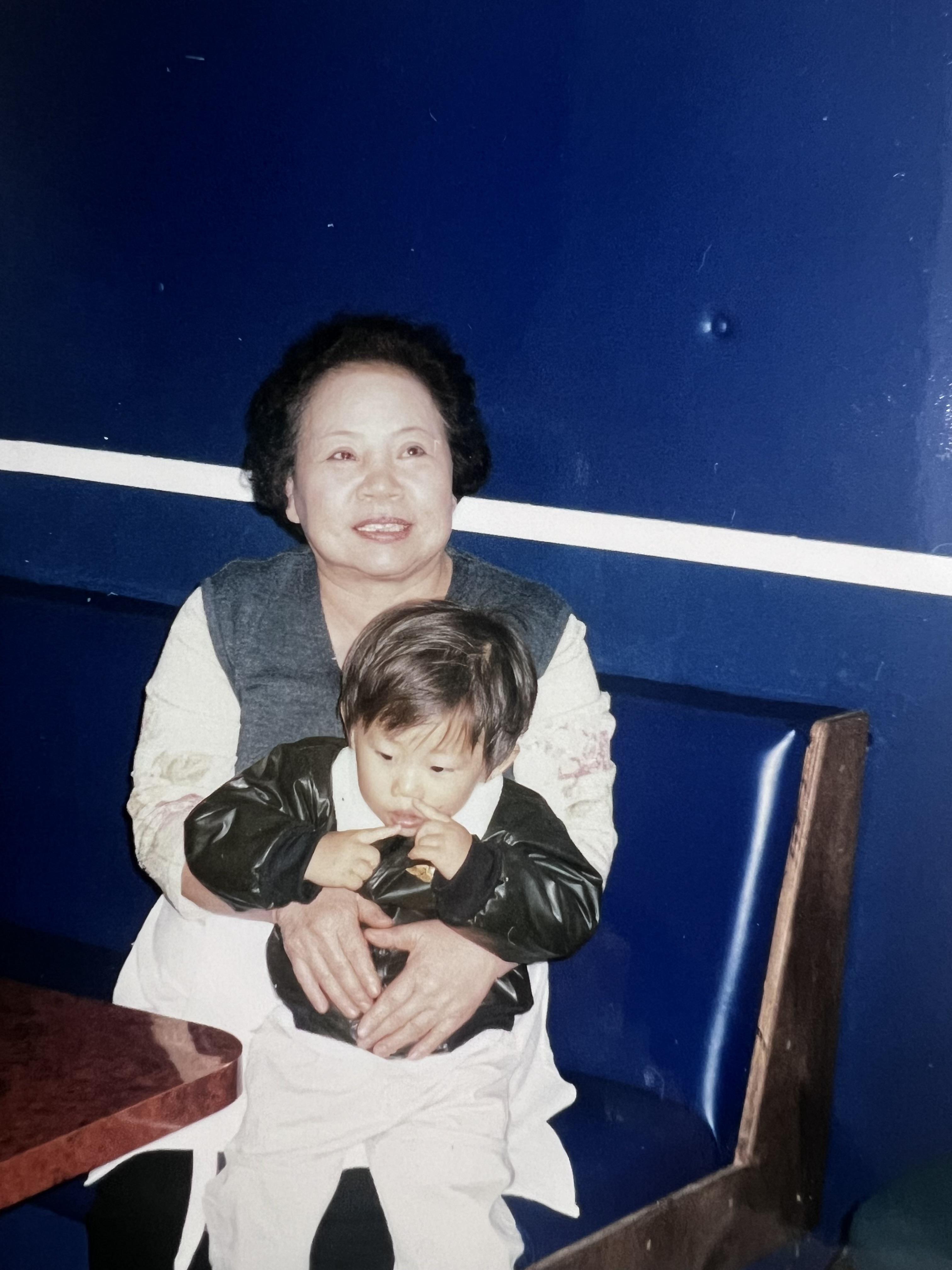 A cheerful grandmother holds a young child in a diner, both smiling happily together.