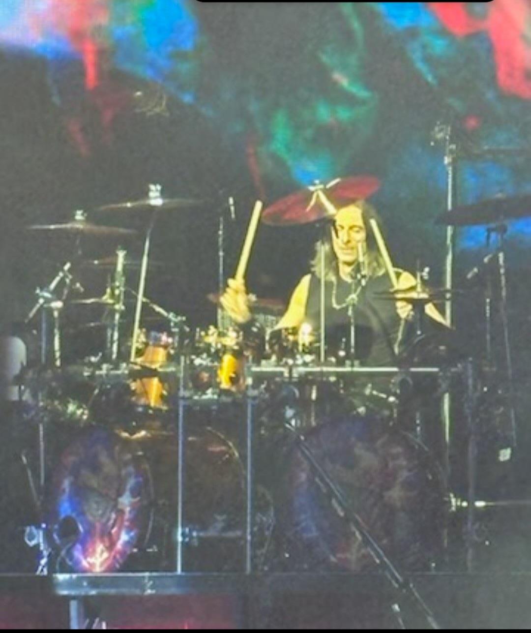 Musician plays drums passionately at a live performance filled with dynamic lighting effects.