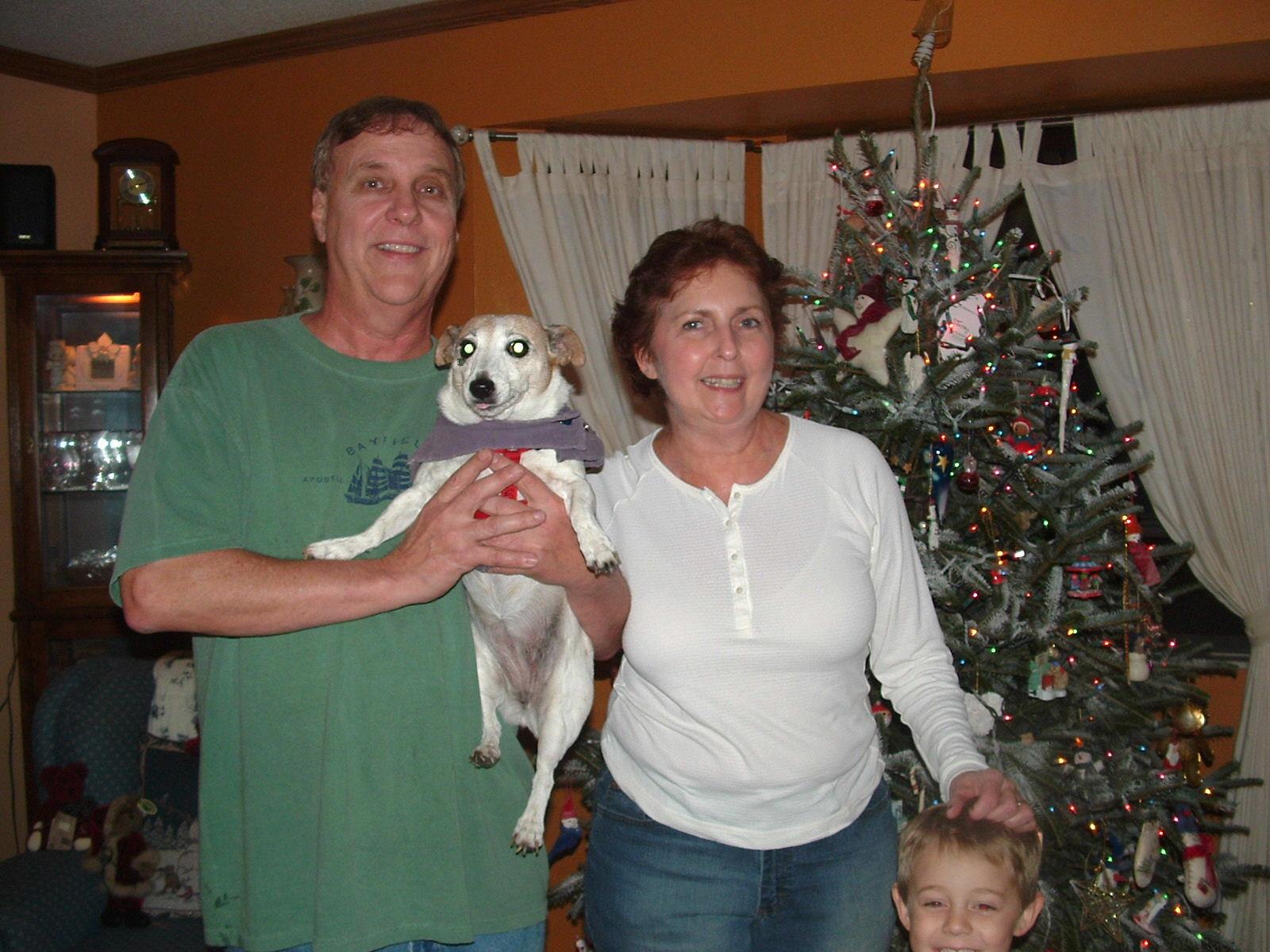 A festive family gathering takes place with a couple holding a dog and a child beside them.