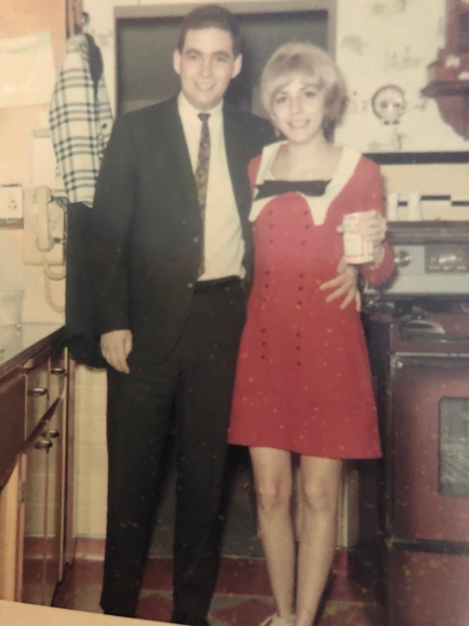 A man and woman stand closely in a vintage kitchen, both dressed stylishly for a memorable event.