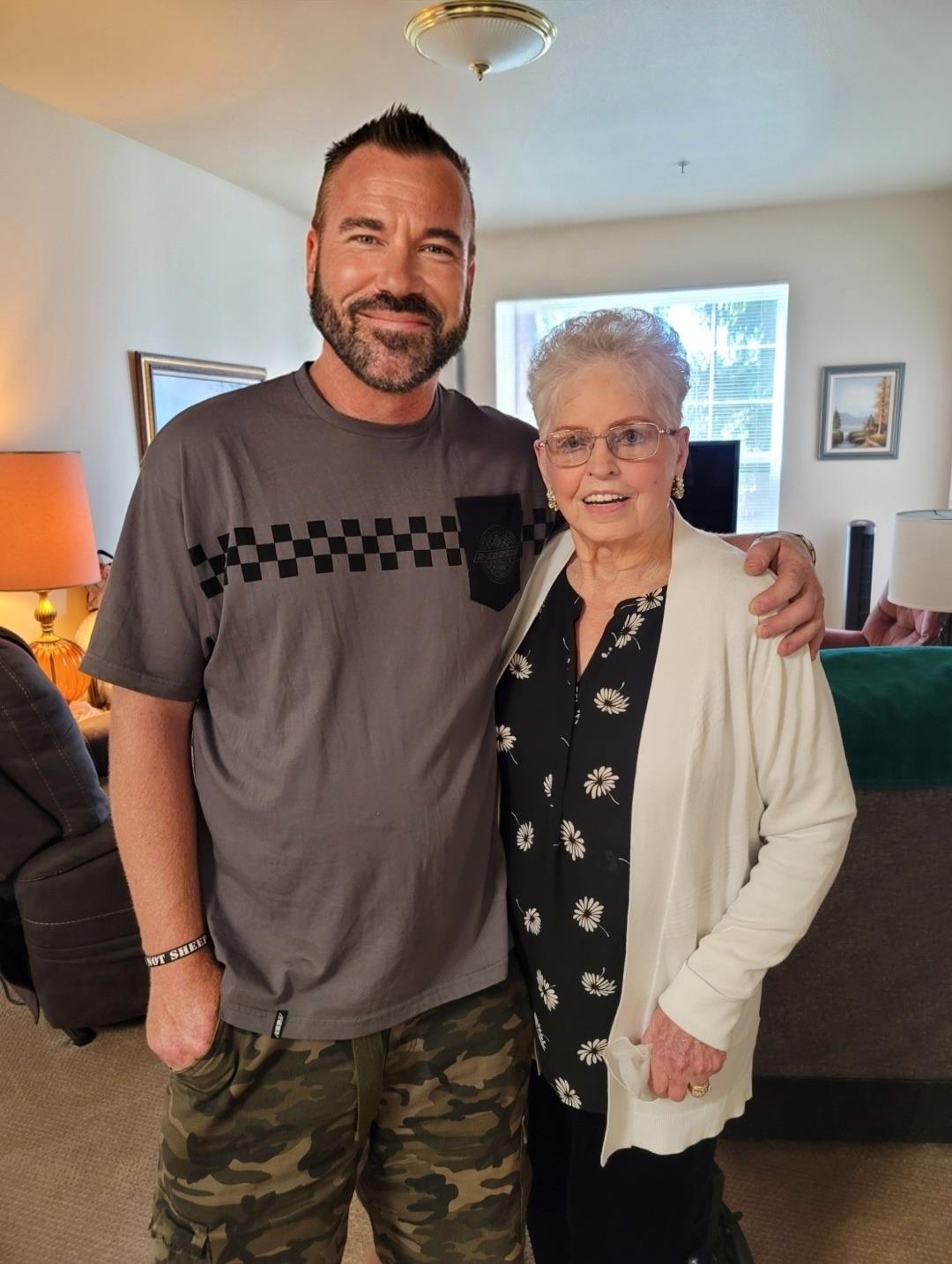 A man and an elderly woman smile together in a cozy living room, showcasing their bond.