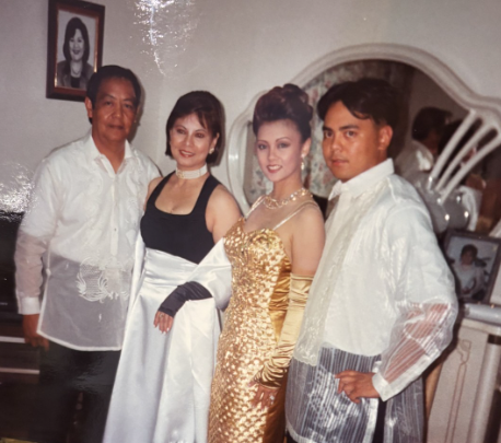Four individuals wearing elegant outfits pose together in a cozy living room filled with decor.