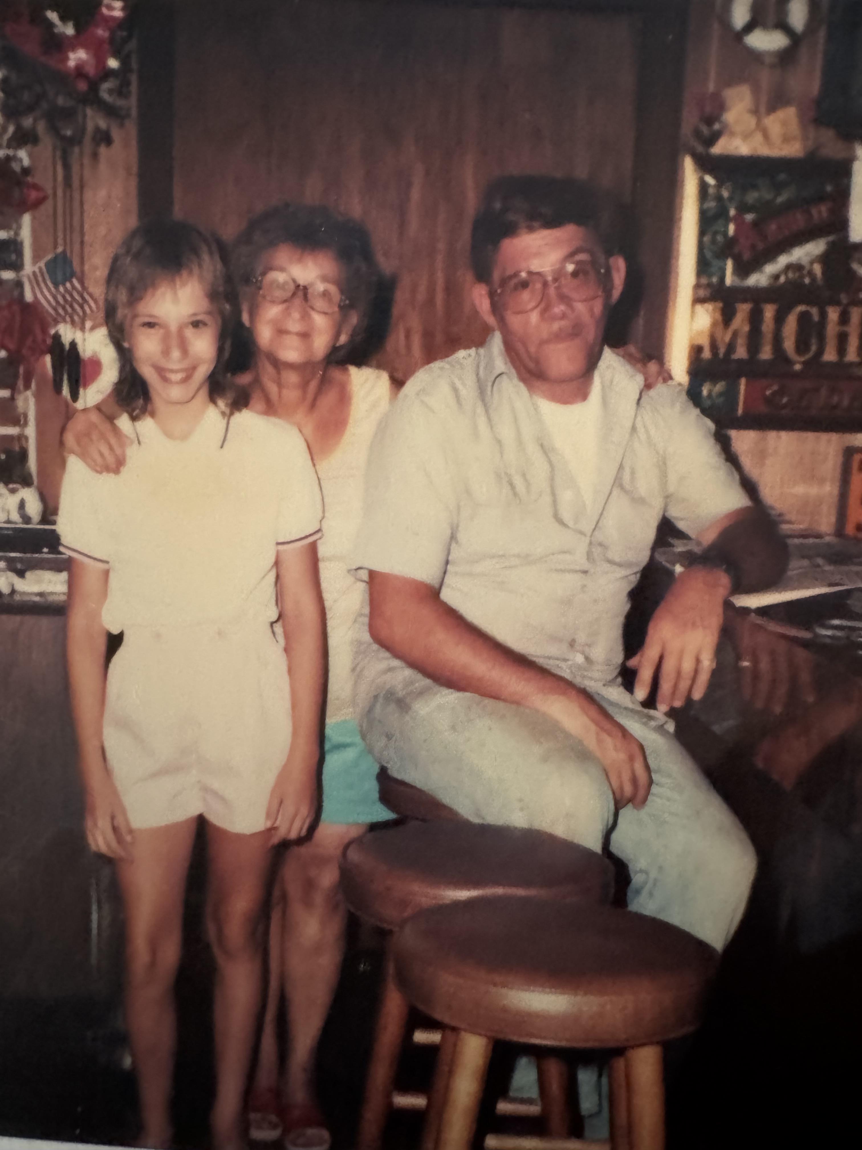 A young girl stands with her grandmother and father in a cheerful kitchen setting.