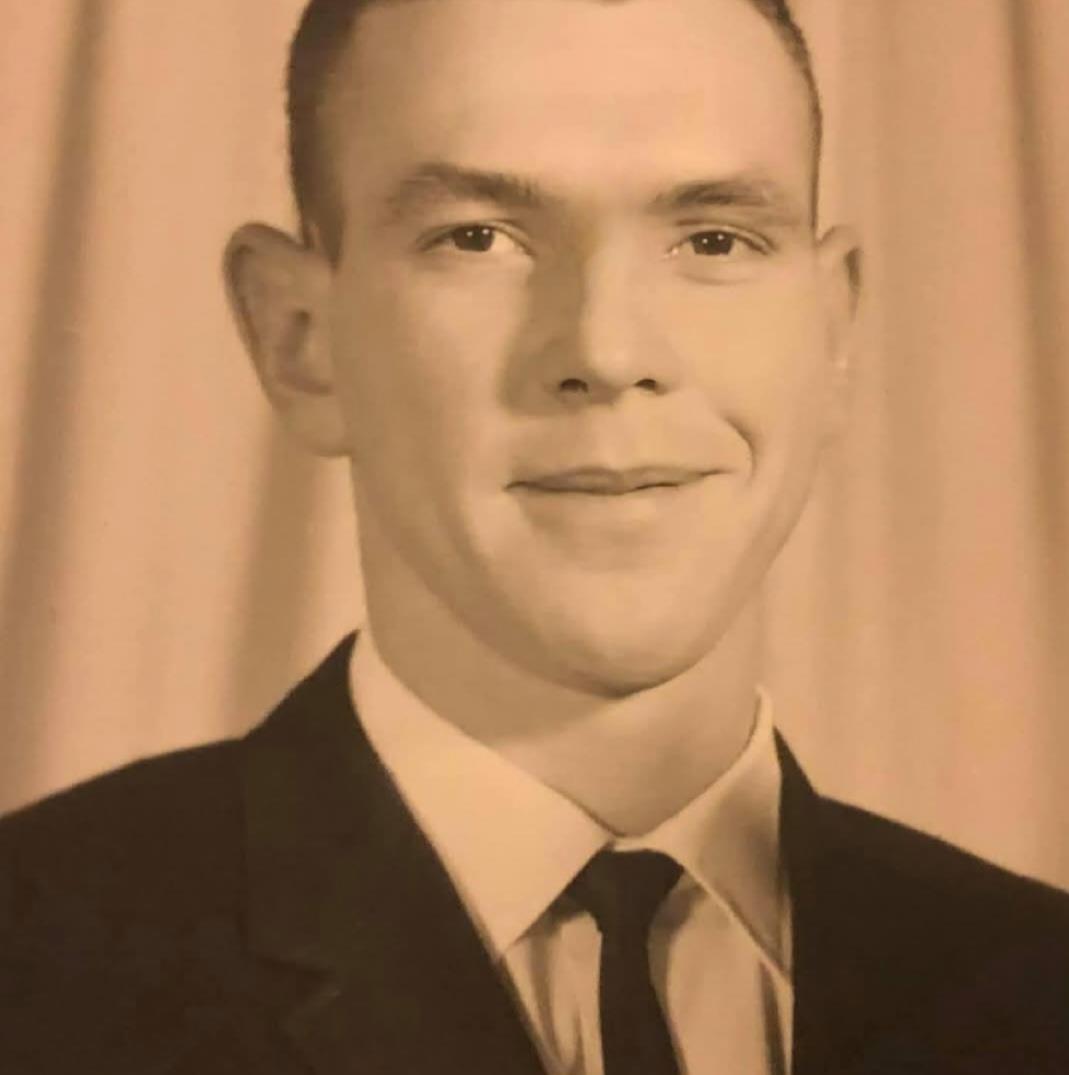 A young man smiles confidently in formal attire against a plain backdrop in a studio.