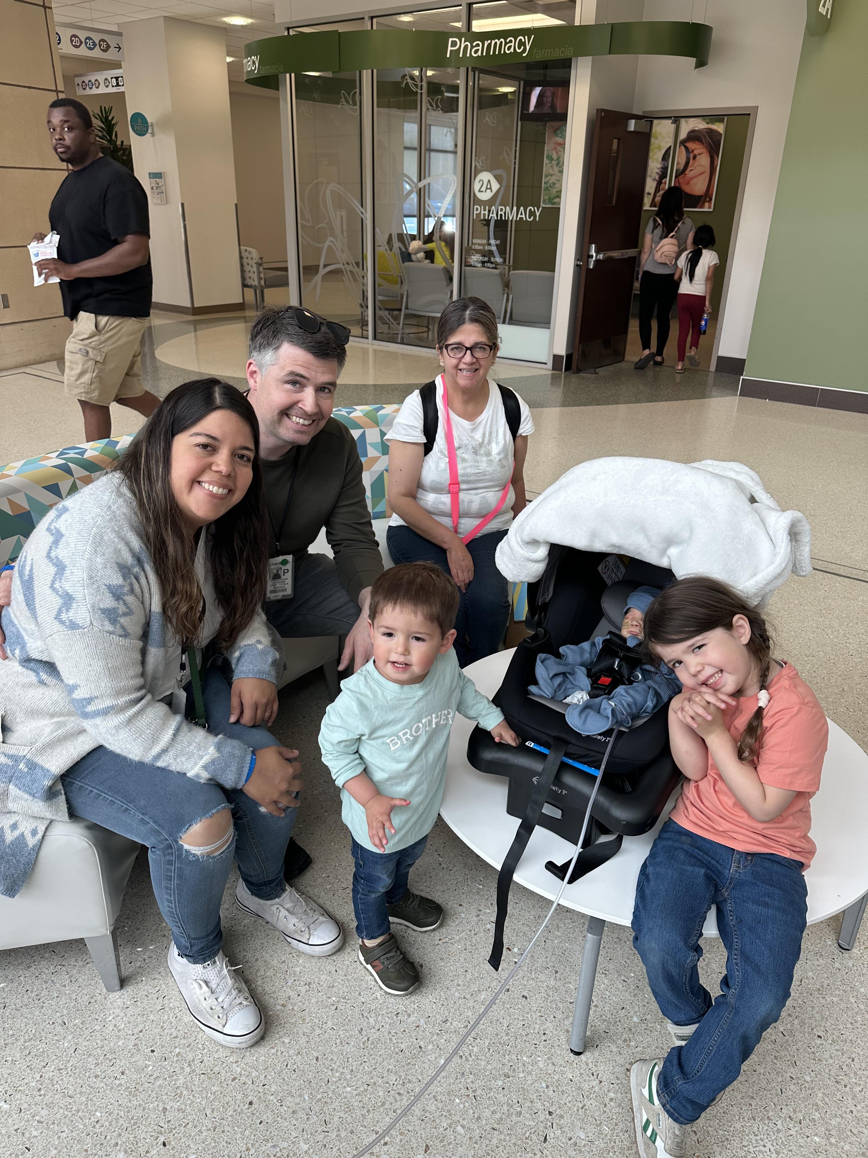 A family enjoys time together in a hospital lobby, celebrating the arrival of a new baby.