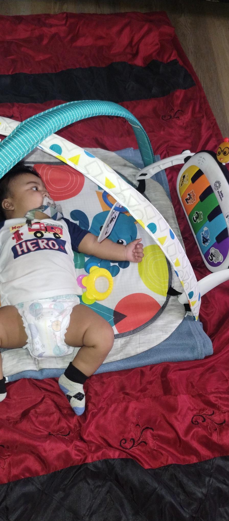 Baby enjoys tummy time on a bright play mat decorated with colorful toys while smiling.