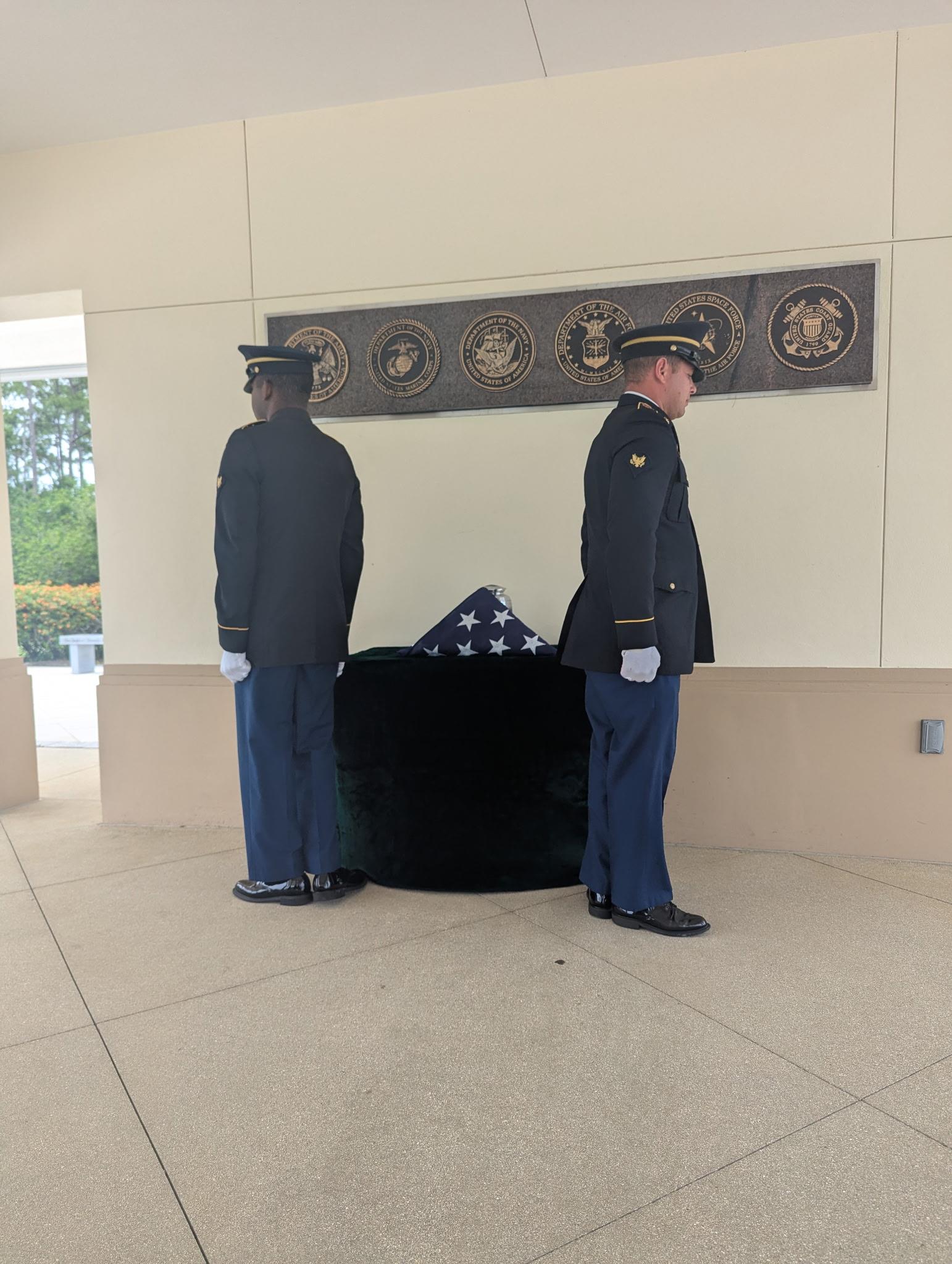 Two honor guards stand at attention near a covered flag, paying tribute at a memorial ceremony.