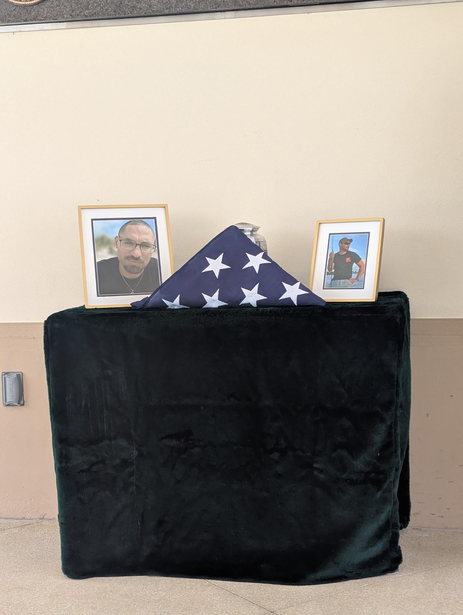 A poignant memorial setup with two framed portraits, a folded flag, and a cozy blanket.
