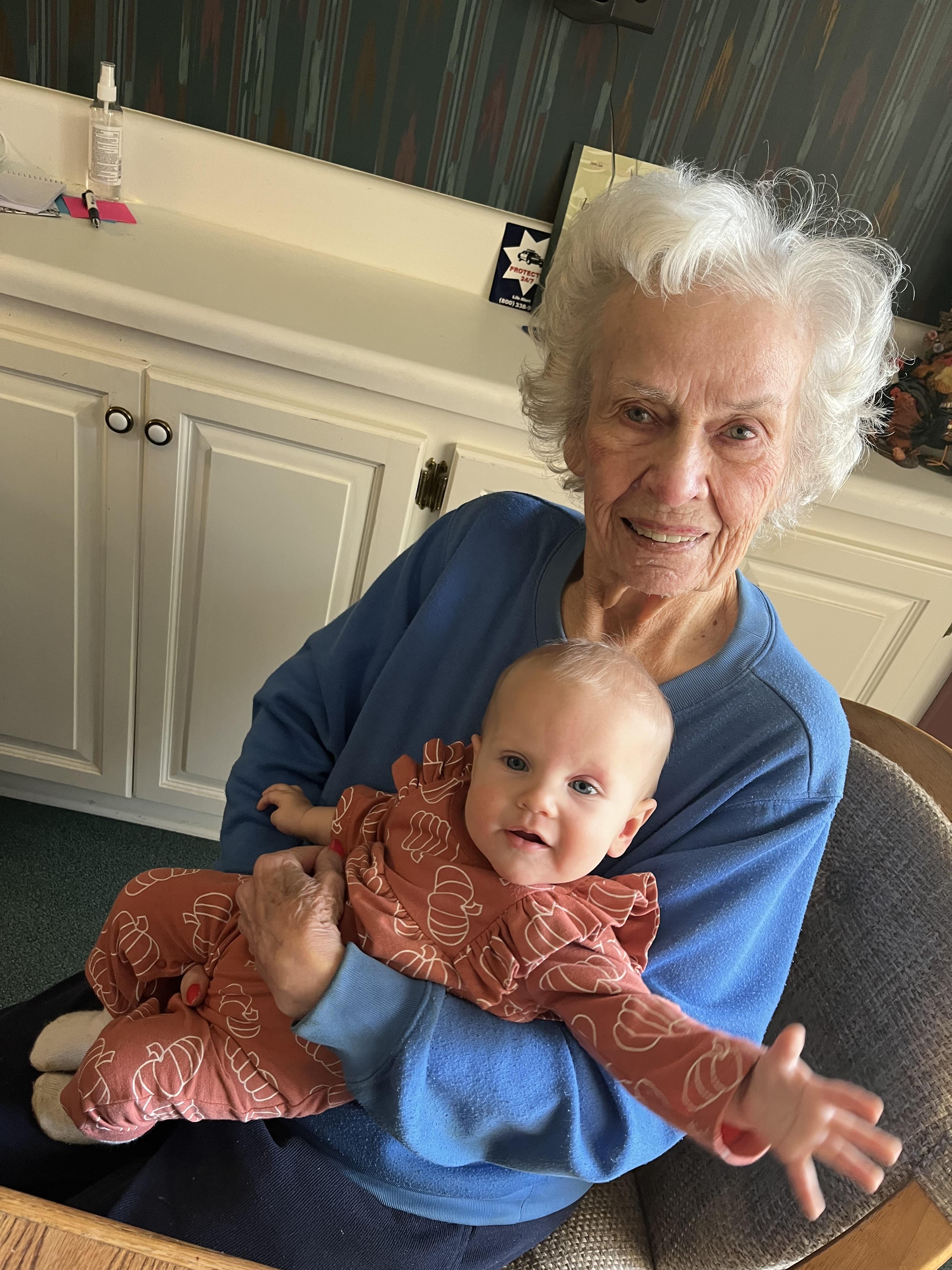 An elderly woman enjoys a joyful moment holding a smiling baby in her lap at home.