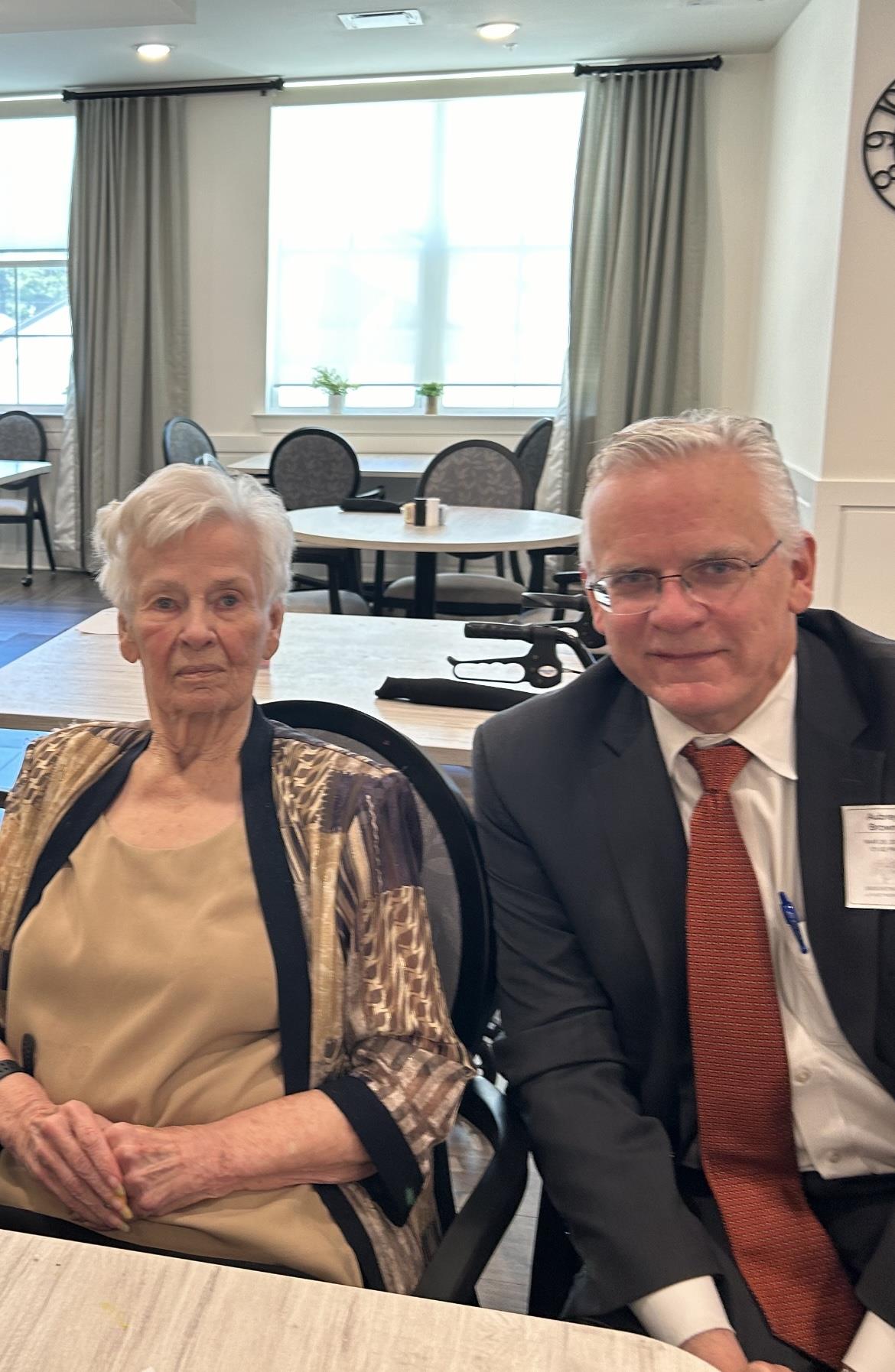 An elderly woman and a man are seated together, engaging warmly in a community setting.