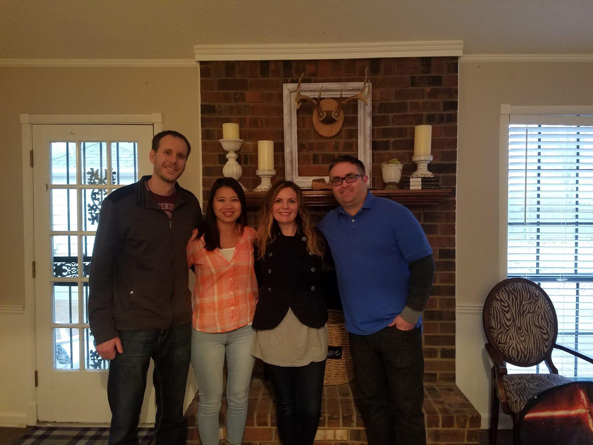 Four friends smile together in a warm living room, sharing laughter and good company at night.