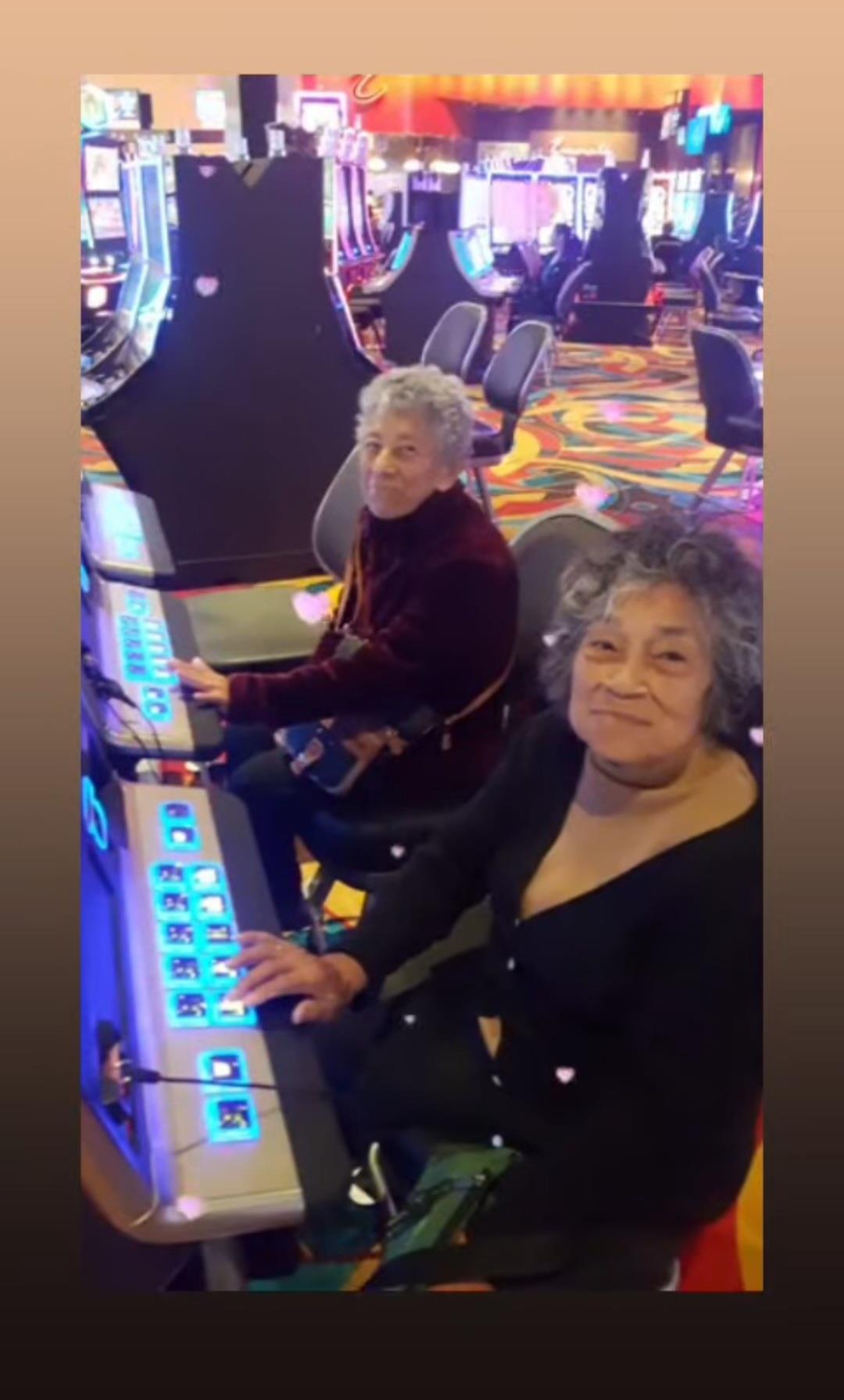 Two elderly women sit at slot machines in a vibrant casino, smiling as they play.