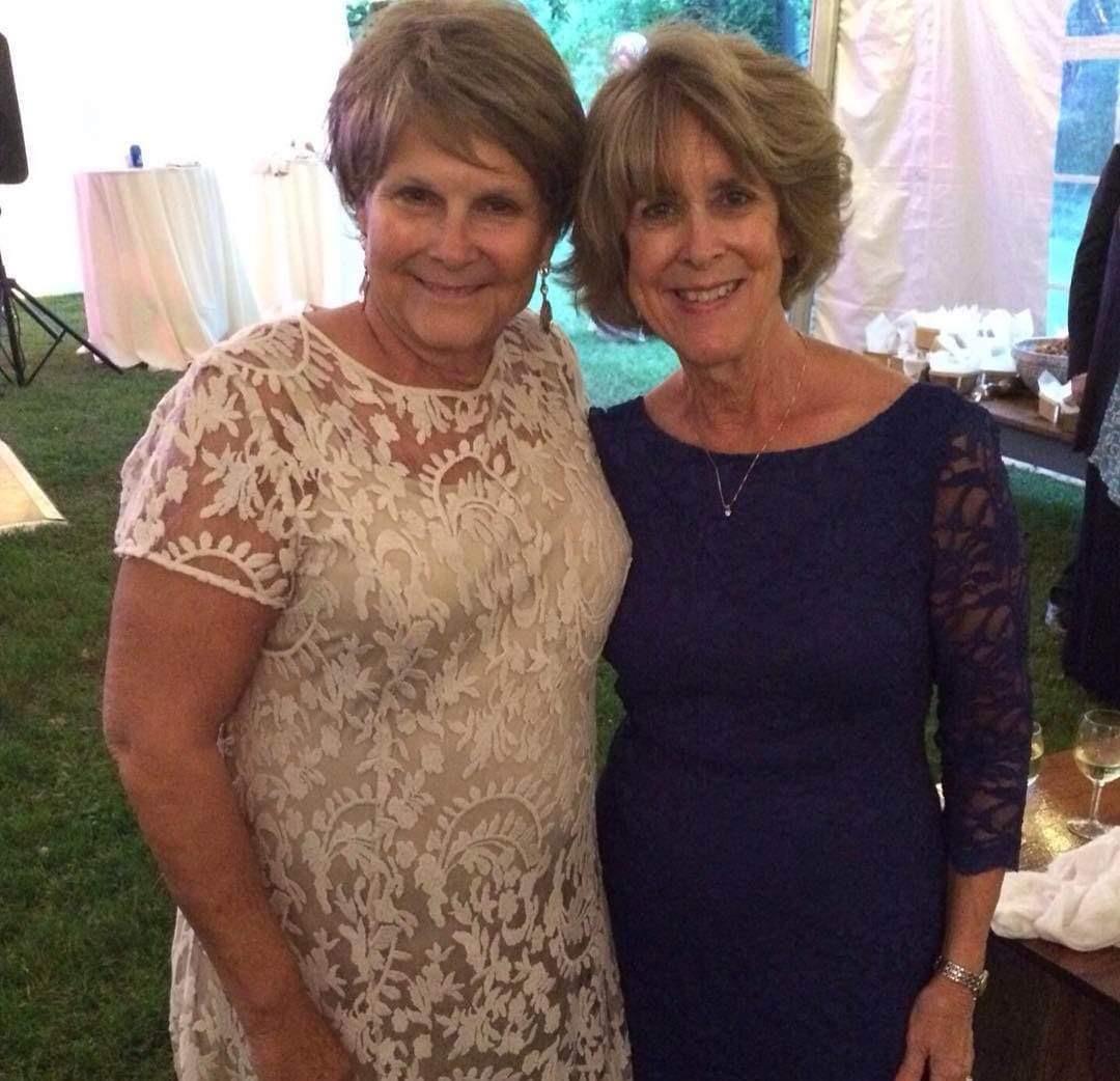 Two women smiling and posing together at a garden celebration in the evening light.