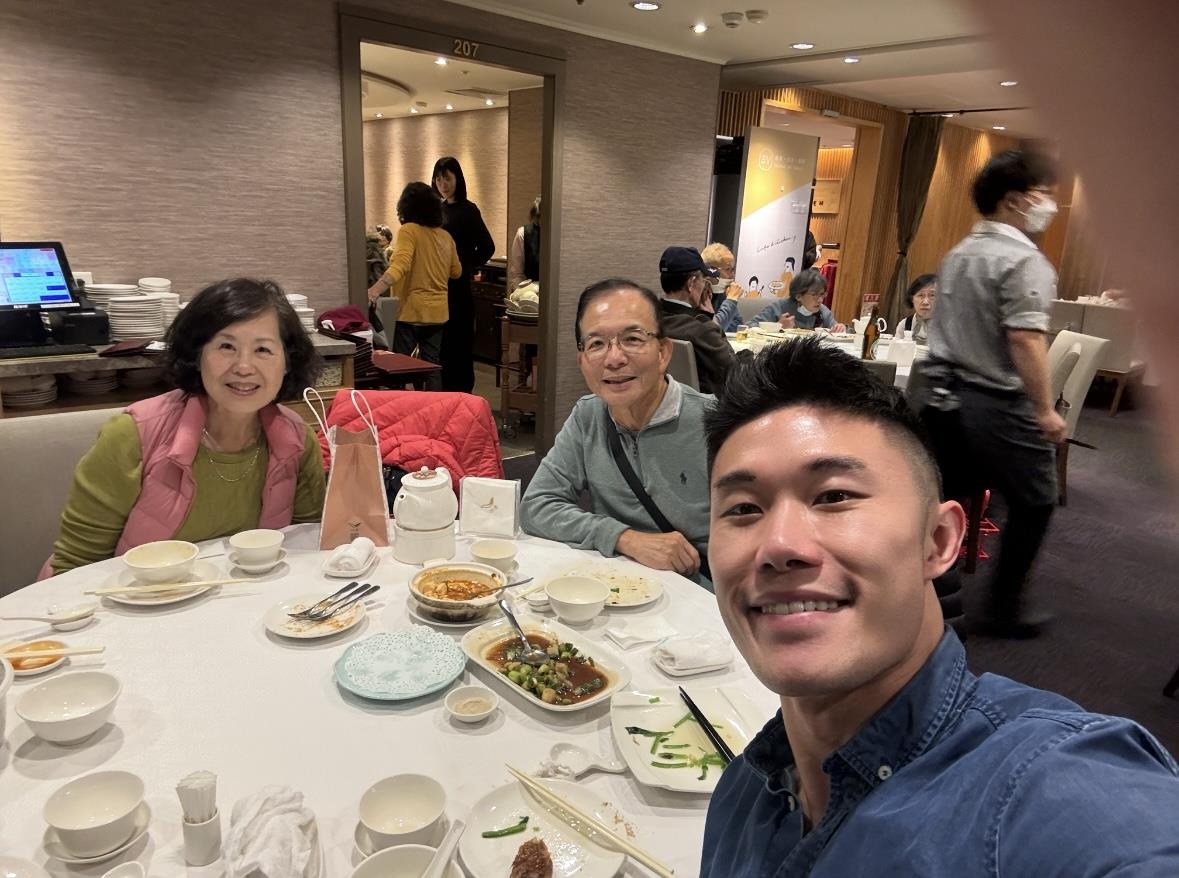 Three people enjoy a meal at a round table in a busy restaurant atmosphere.