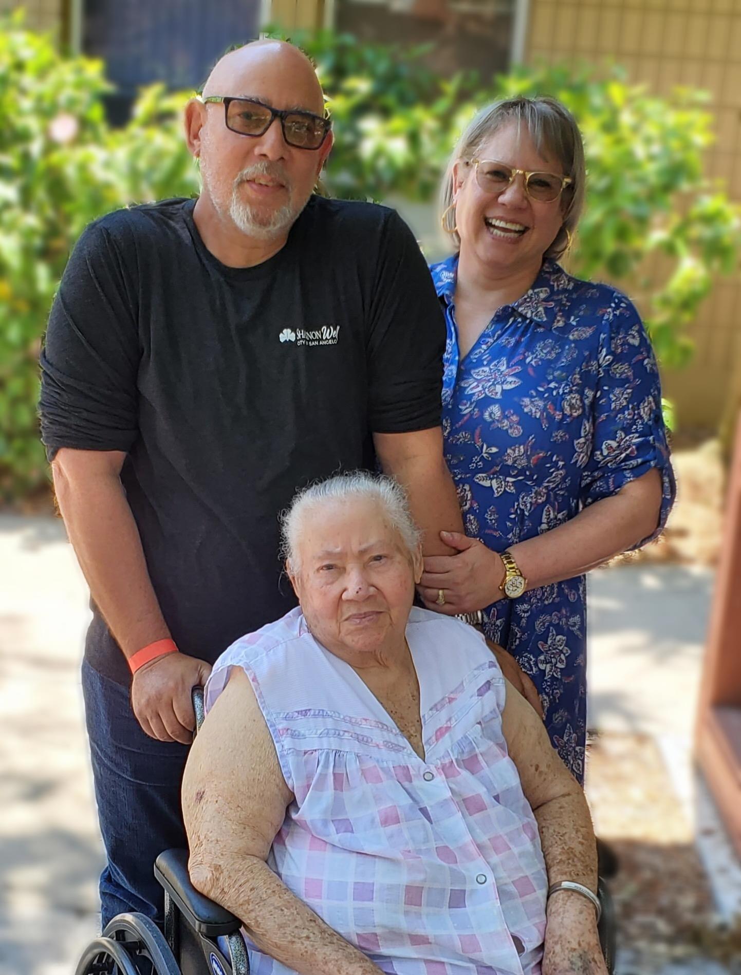 Family members hug their elder outside, expressing love and connection on a sunny day.
