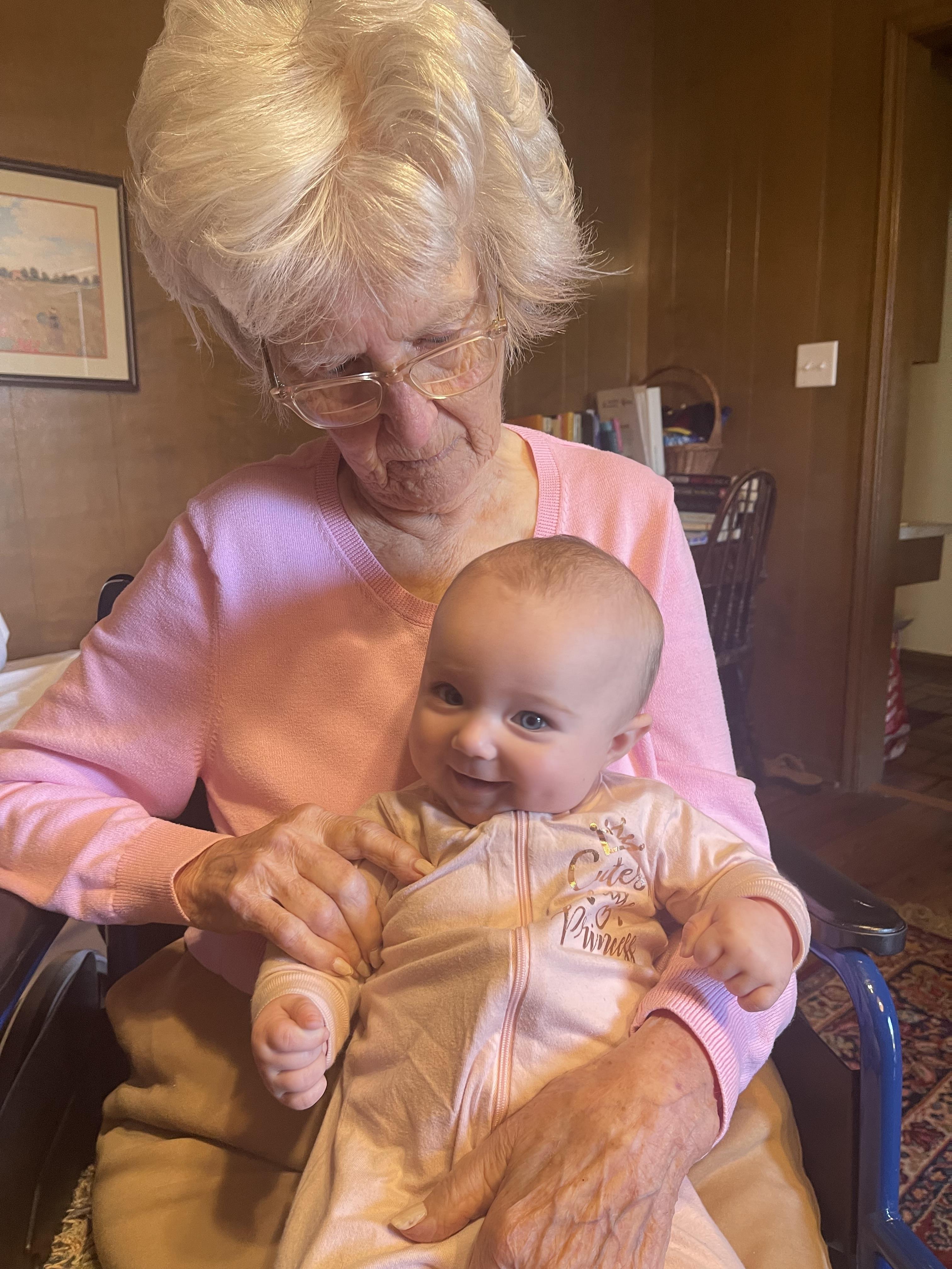 Elderly woman smiles while holding a happy baby in a warm, inviting room during the afternoon.