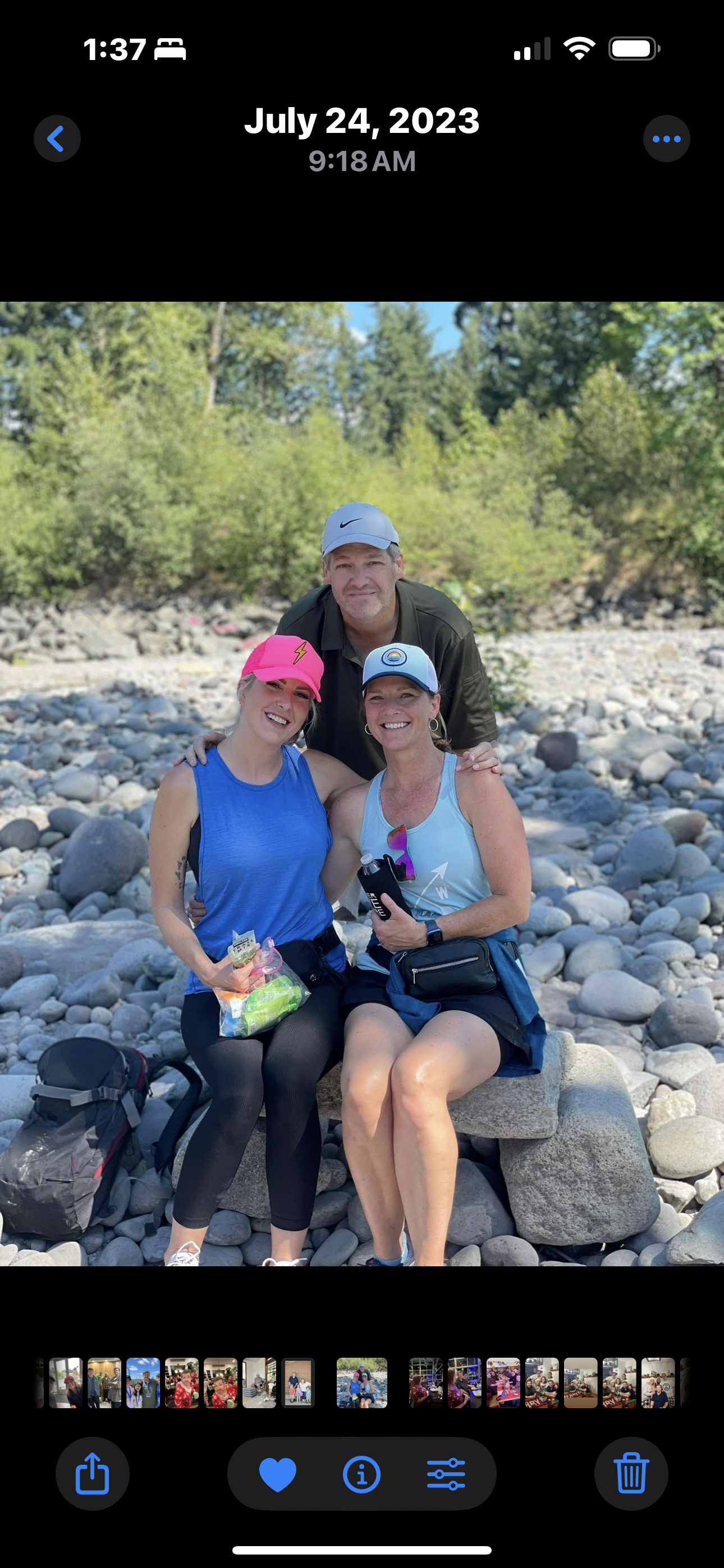 Three friends relax by the river, enjoying snacks and each other's company on a sunny day.