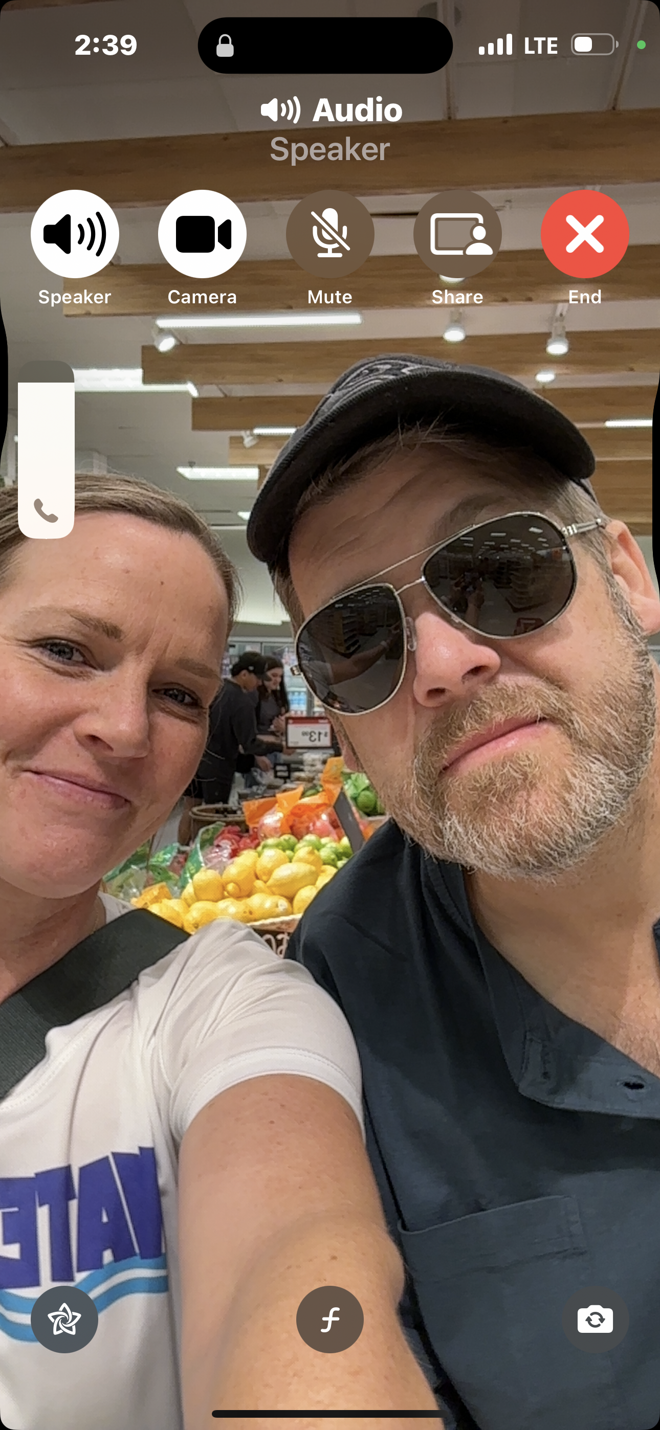 Two friends take a selfie together in a lively market surrounded by colorful fruits.