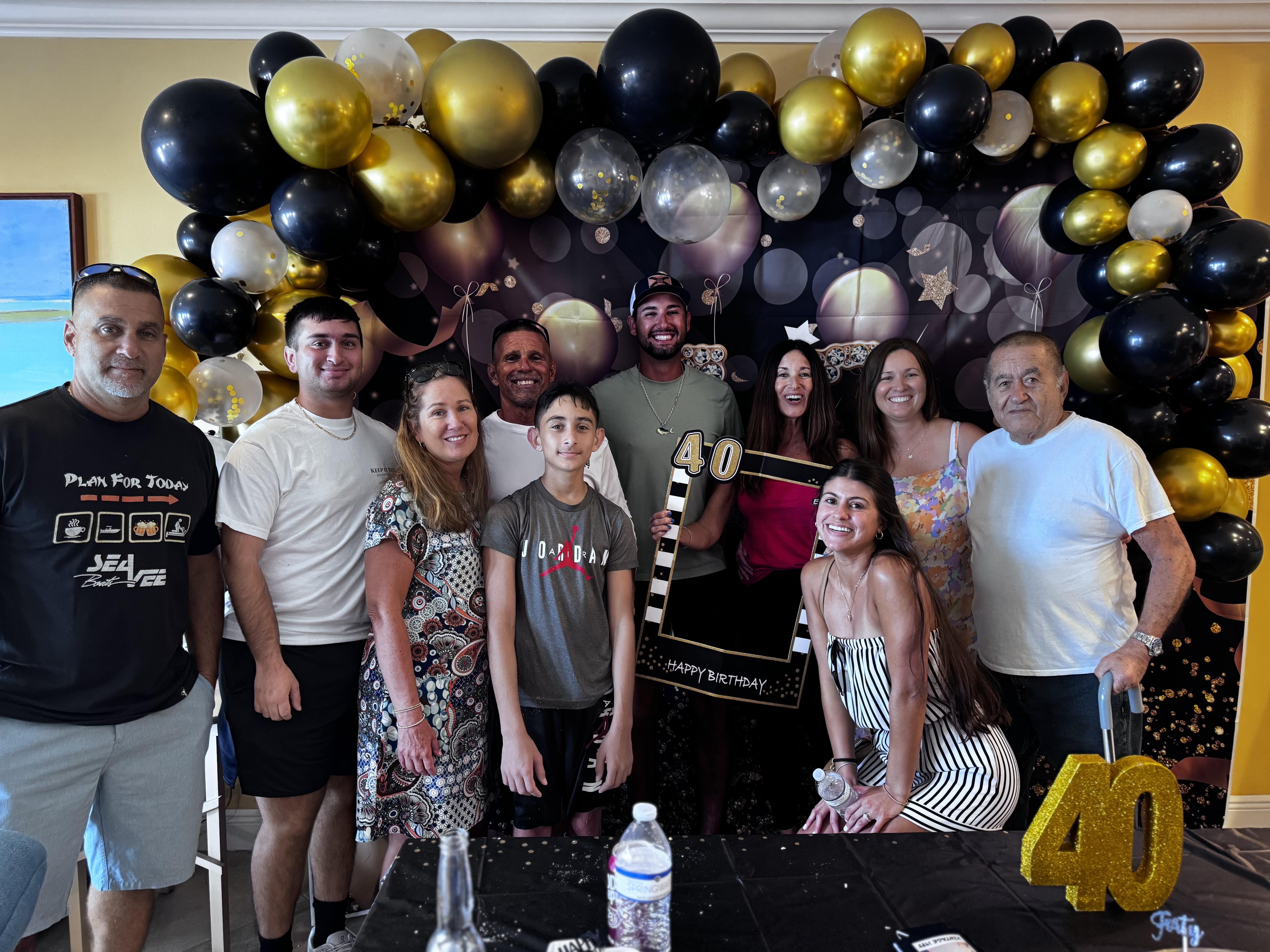 Group of family and friends celebrating a special occasion among festive black and gold decorations.