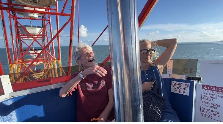 Two individuals share laughter on a Ferris wheel overlooking the ocean during an afternoon outing.