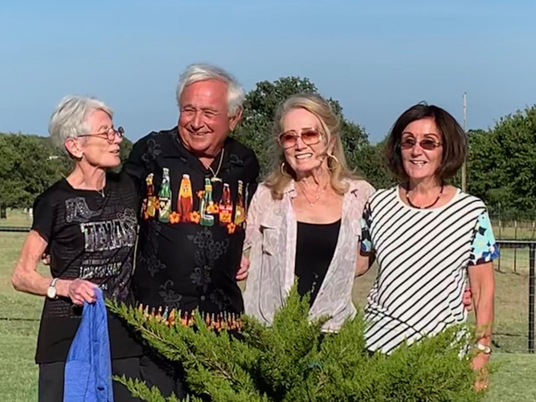 Four friends joyfully pose together outdoors on a sunny day, enjoying each other’s company.