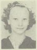 Child with curly hair poses for a school portrait in a classroom, showing her cheerful expression.