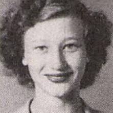 A young woman with curly hair smiles warmly at the camera, showcasing her joyful expression.