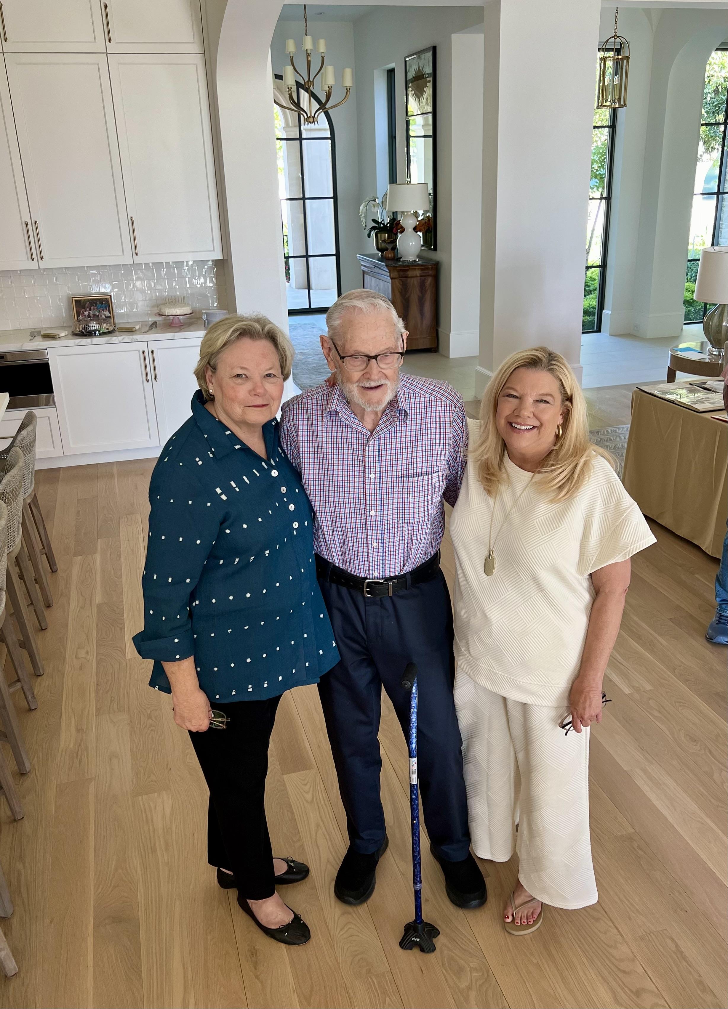 Three adults joyfully pose in a contemporary living room filled with natural light.